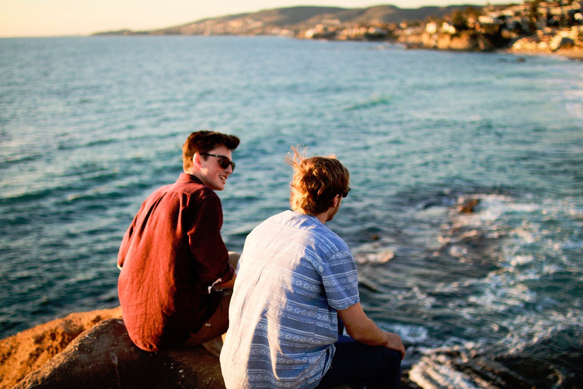 Pictured - Two men conversing while sitting on rocks near the ocean | Source: Pixabay