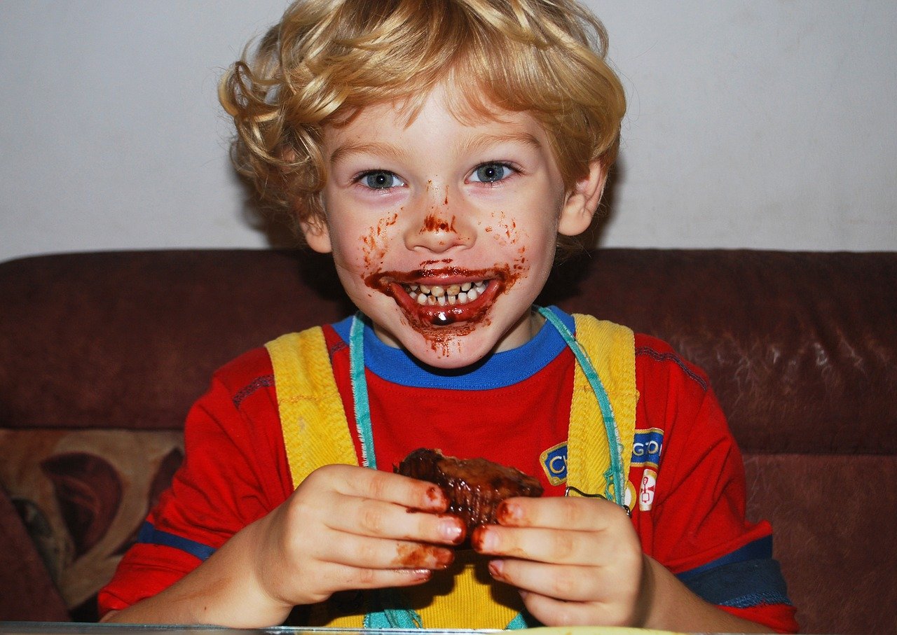A little boy smiling broadly while his mouth is smeared with juices from the meat he’s eating | Photo: Pixabay/Mojpe