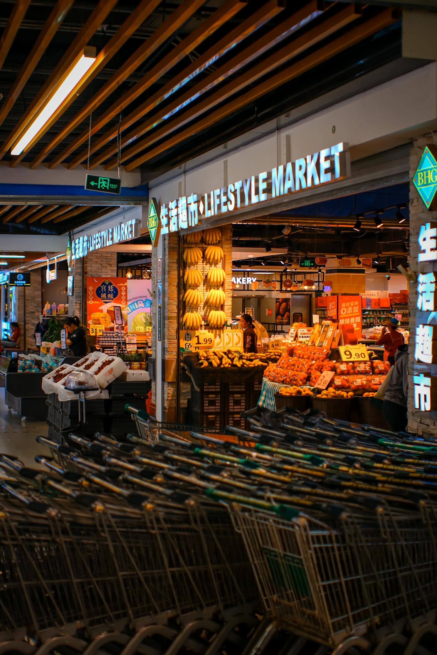 Rows of neatly stacked shopping trolleys sit in the foreground of a brightly lit supermarket | Source: Pexels
