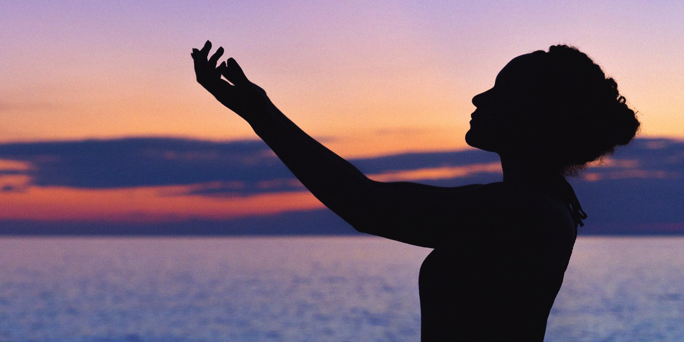 A woman's silhouette in front of a sun setting by the ocean | Image: AmoDays