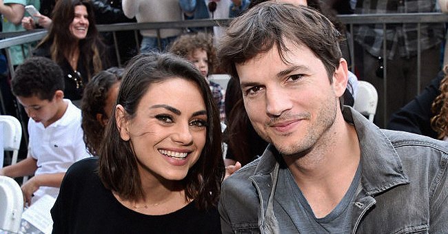 Mila Kunis and Ashton Kutcher smile for a photo while watching an outdoor event. | Source: Getty Images