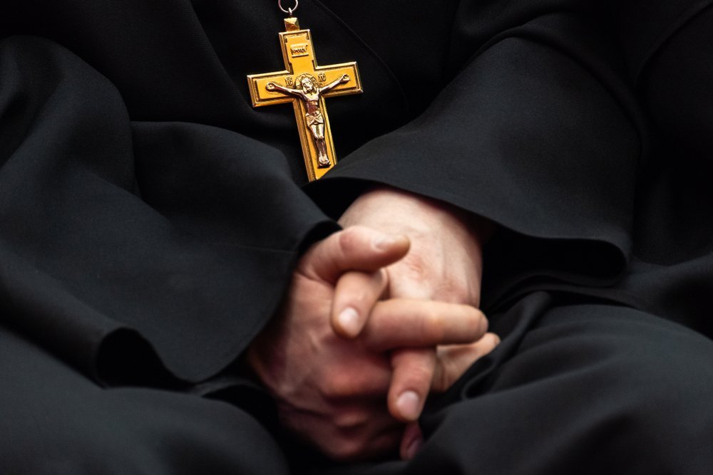 Golden cross with crucifixion of Jesus on the chest of a priest in black clothes | Photo: Shutterstock