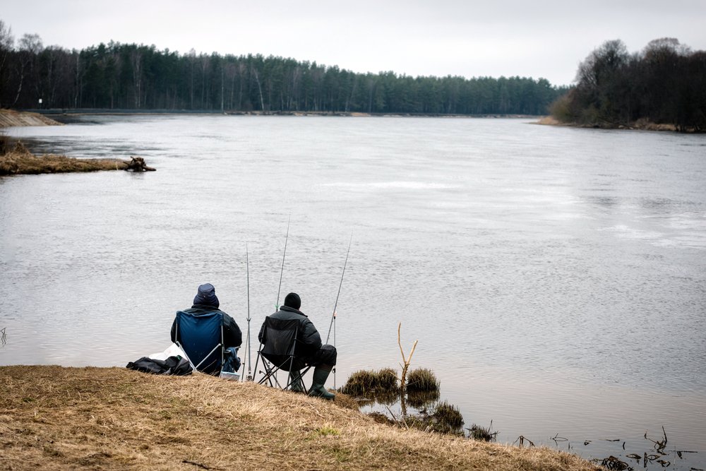 Two men sitting with a pole and catching fish from the lake shore. | Photo: Shutterstock.