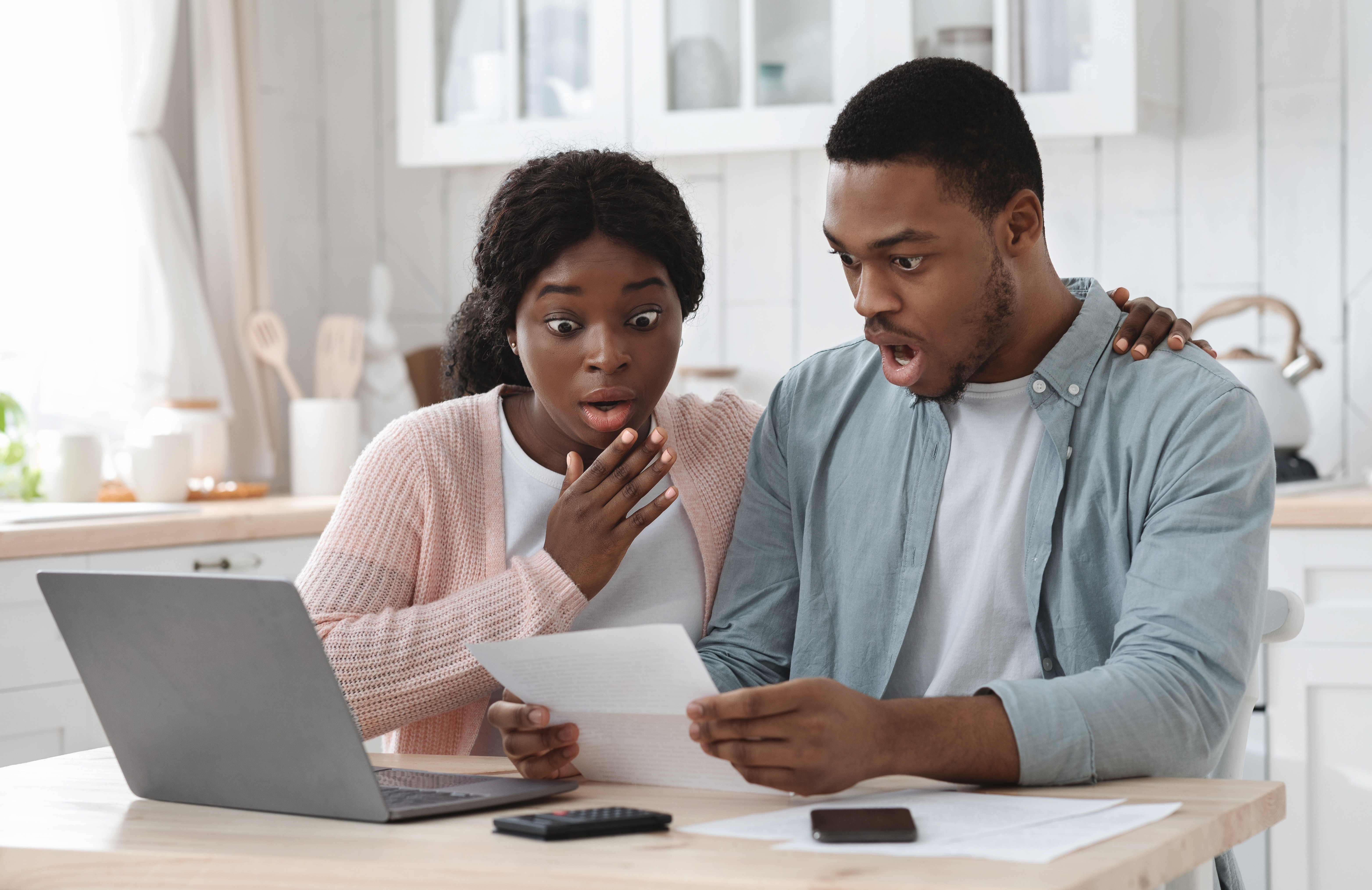 Shocked black couple in kitchen having financial problems, doing family budget calculations | Source: Getty Images