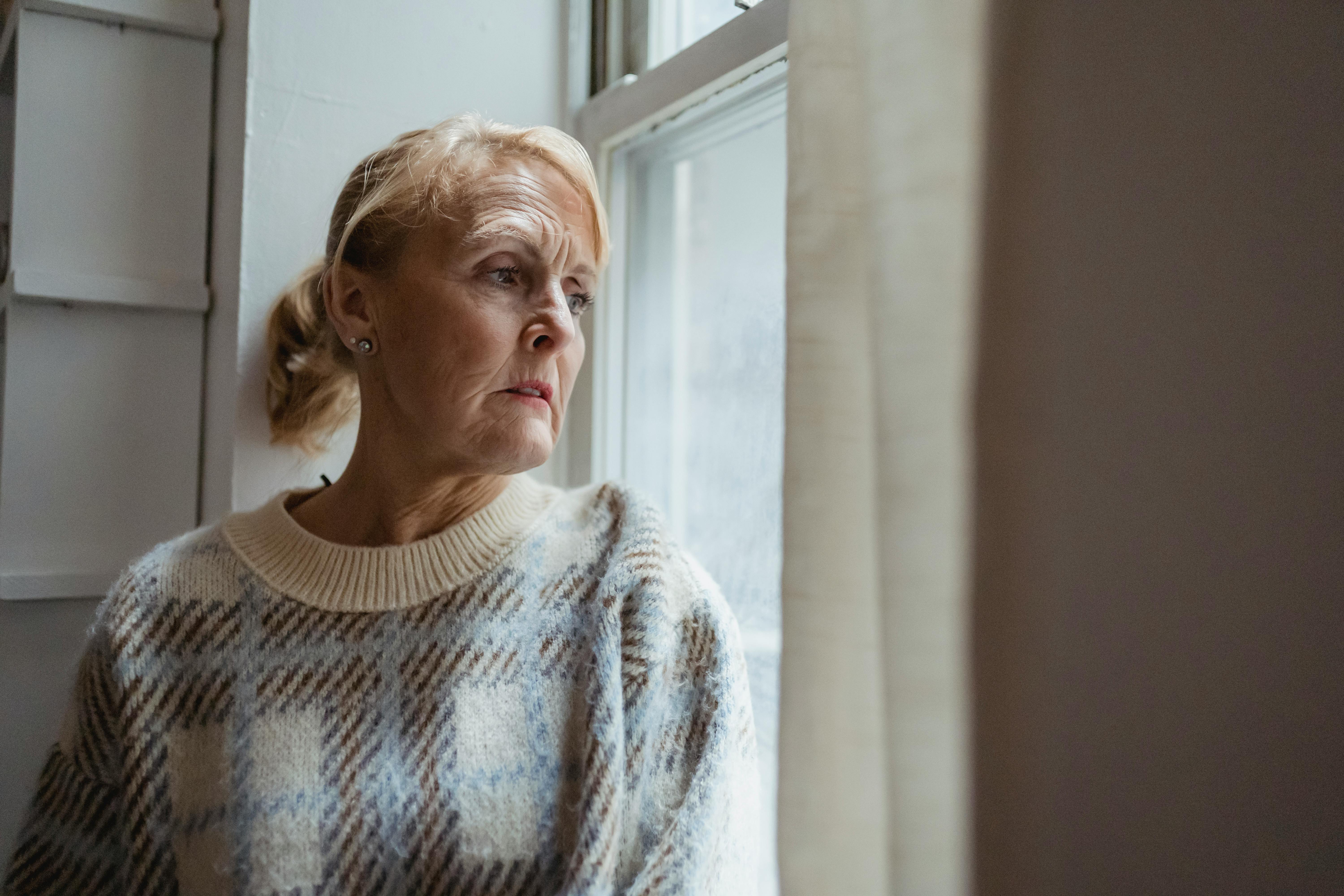 An older woman looking sad while looking outside a window | Source: Pexels