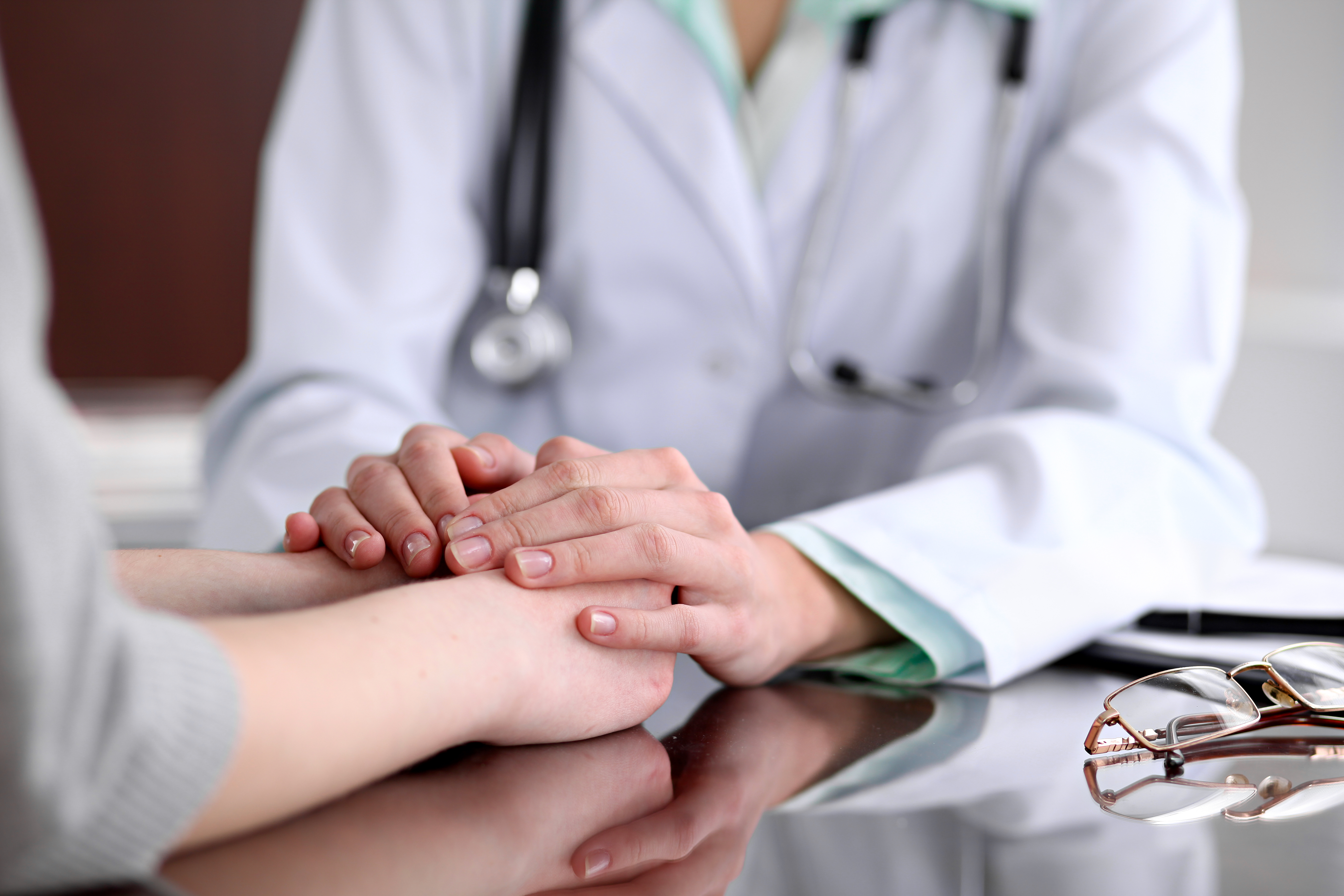 Friendly female doctor hands holding patient hand sitting at the desk for encouragement, empathy, cheering and support while medical examination. | Source: Shutterstock