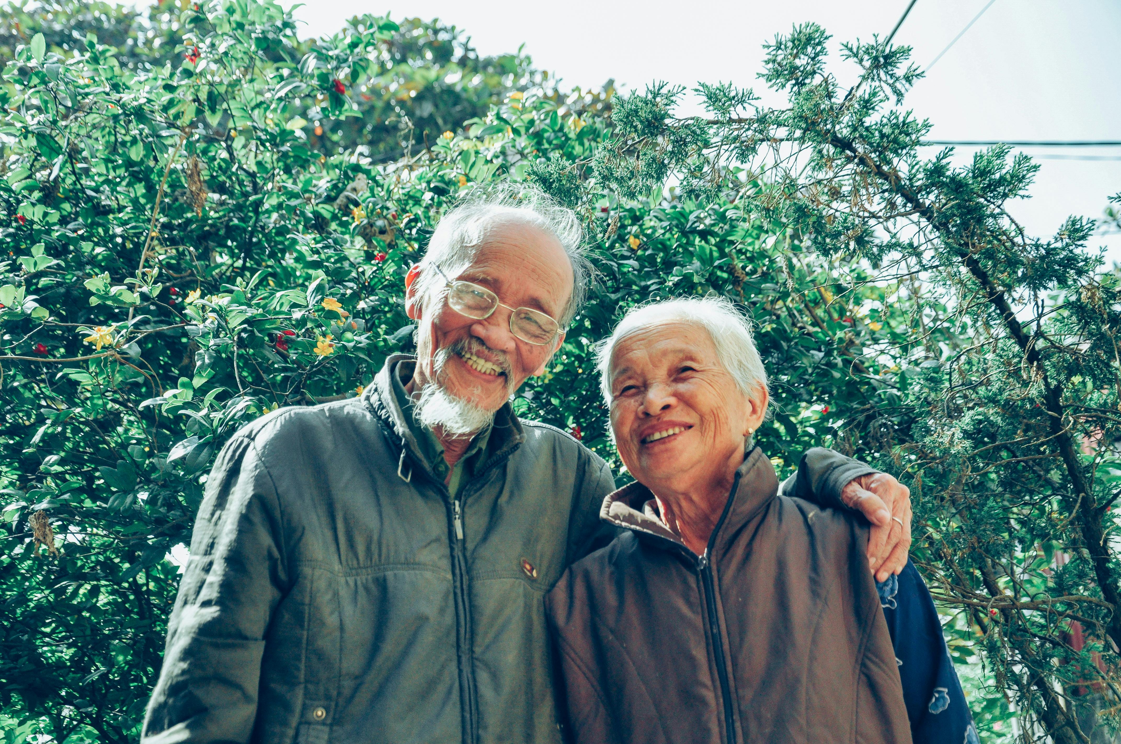 An older couple smiles together while standing outdoors in a garden. | Source: Pexels