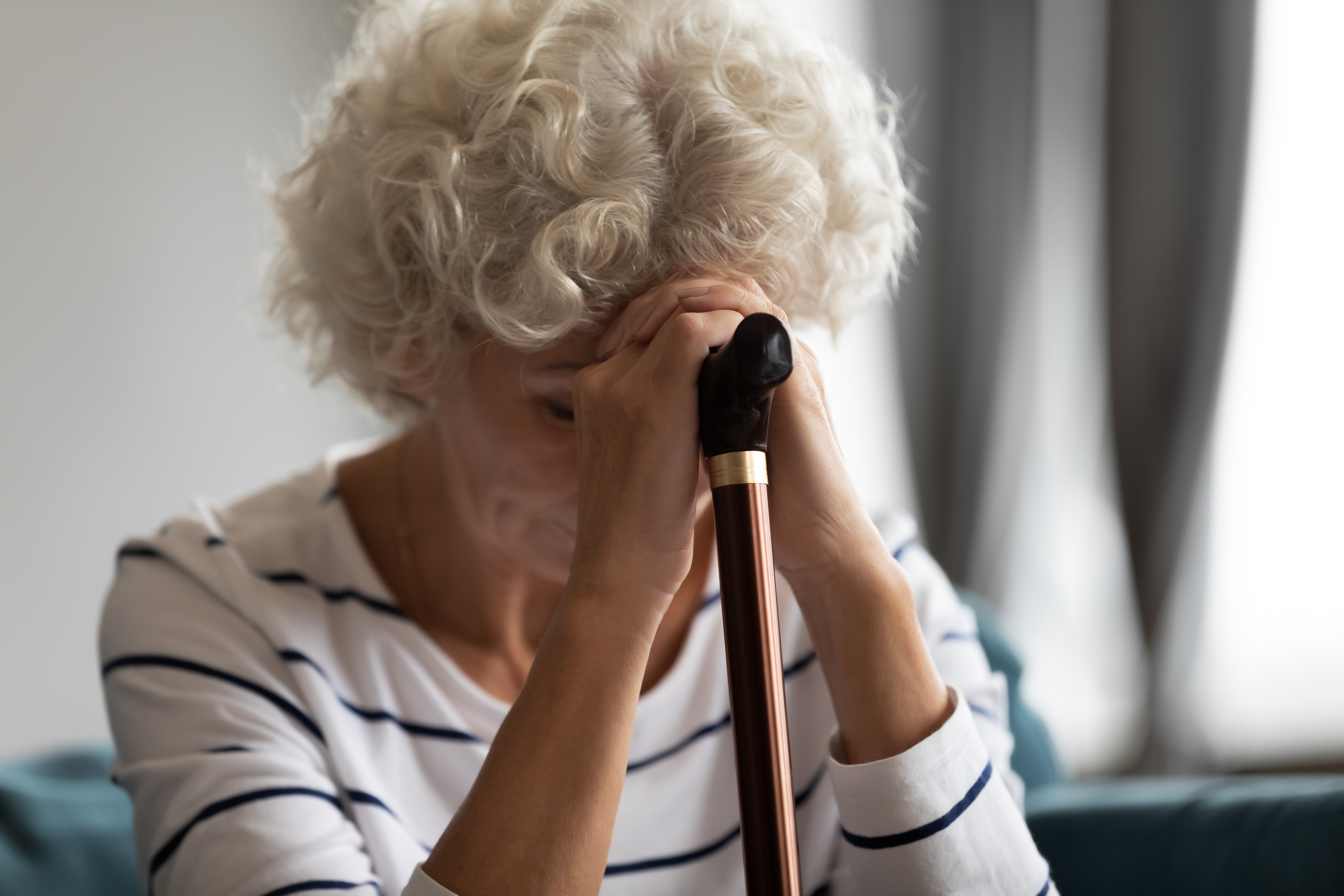 A sad woman balancing her hands and head on a walking cane | Source: Shutterstock
