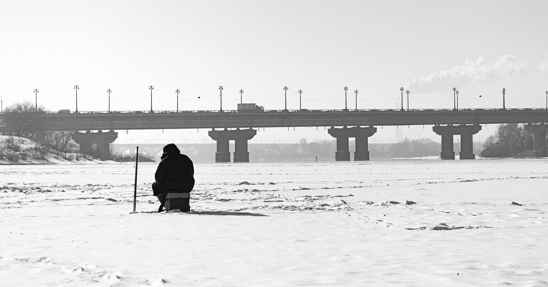 A man ice fishing in a frozen over river. | Photo: Pixabay.