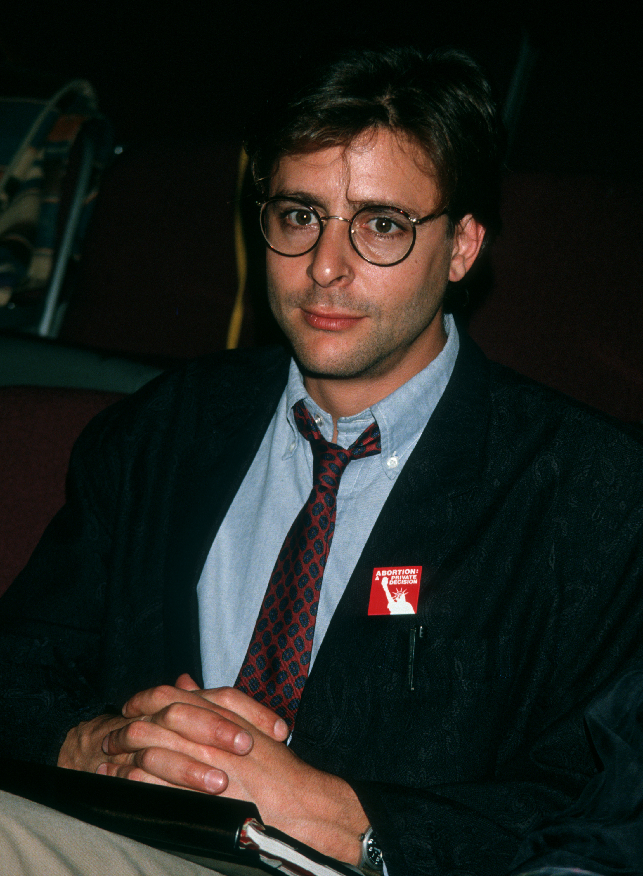 Seated with hands clasped during the first rehearsal for the stage play "Carnal Knowledge" at the Kaufman Theater in New York City, the actor paired round-framed glasses and a patterned tie with an advocacy pin on his blazer lapel. | Source: Getty Images