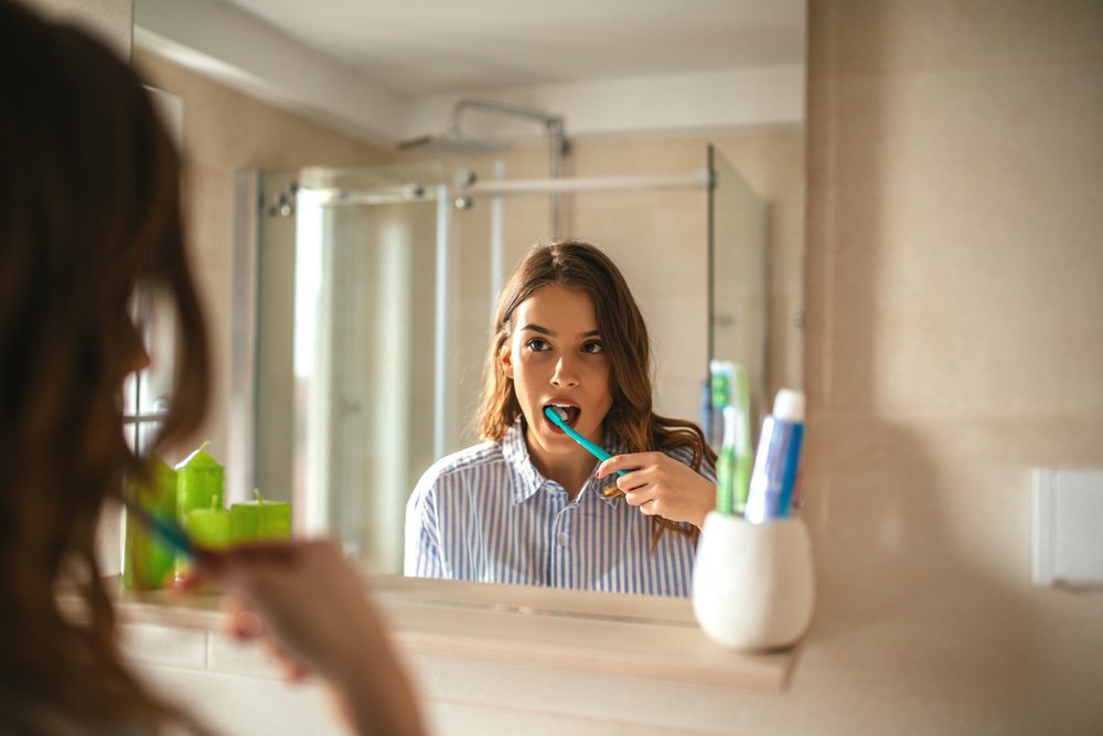 Mujer mirándose al espejo mientras se cepilla los dientes. | Foto: Shutterstock