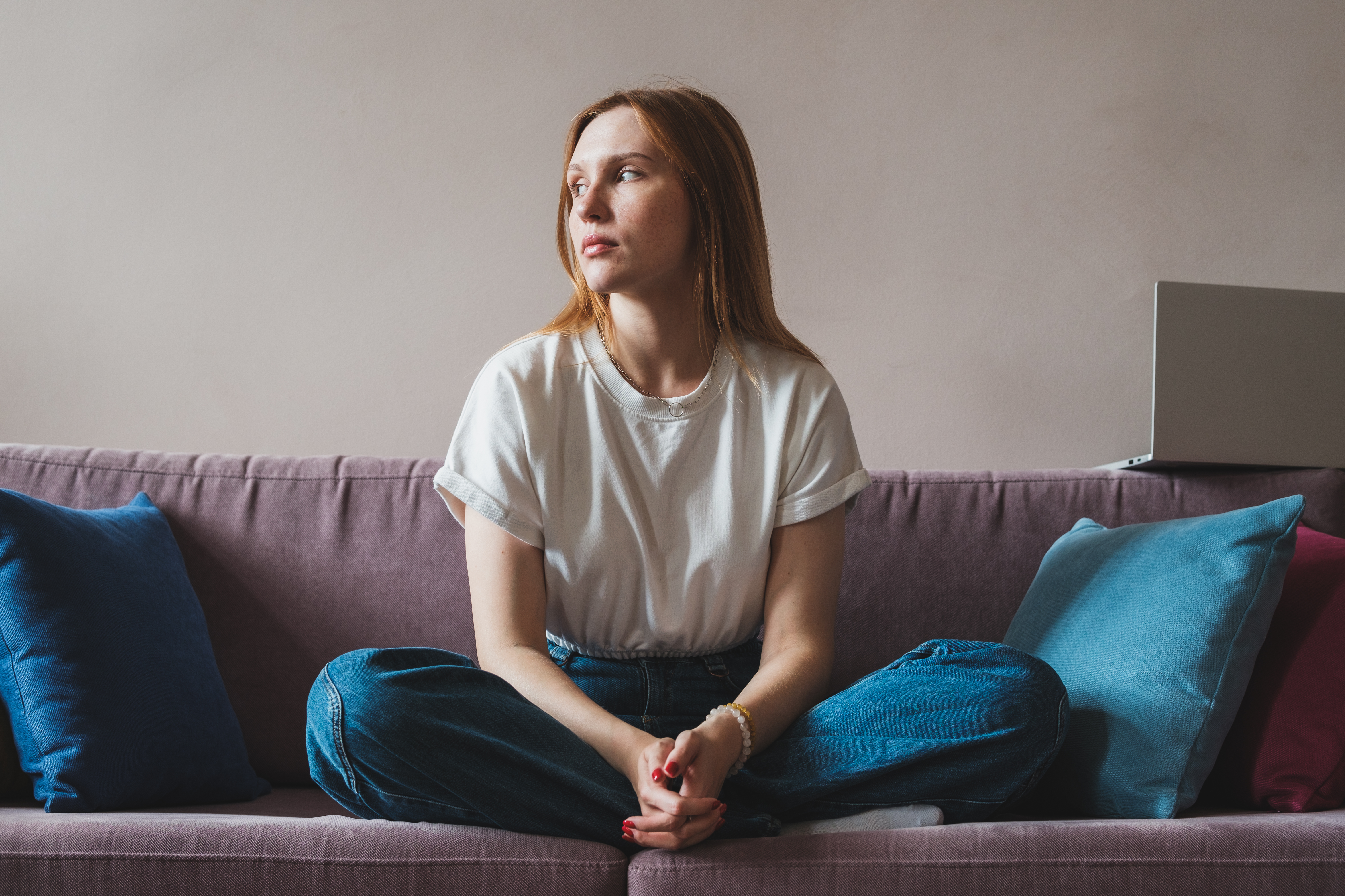 Upset depressed young woman freelancer sitting on sofa with laptop looking out window | Source: Getty Images