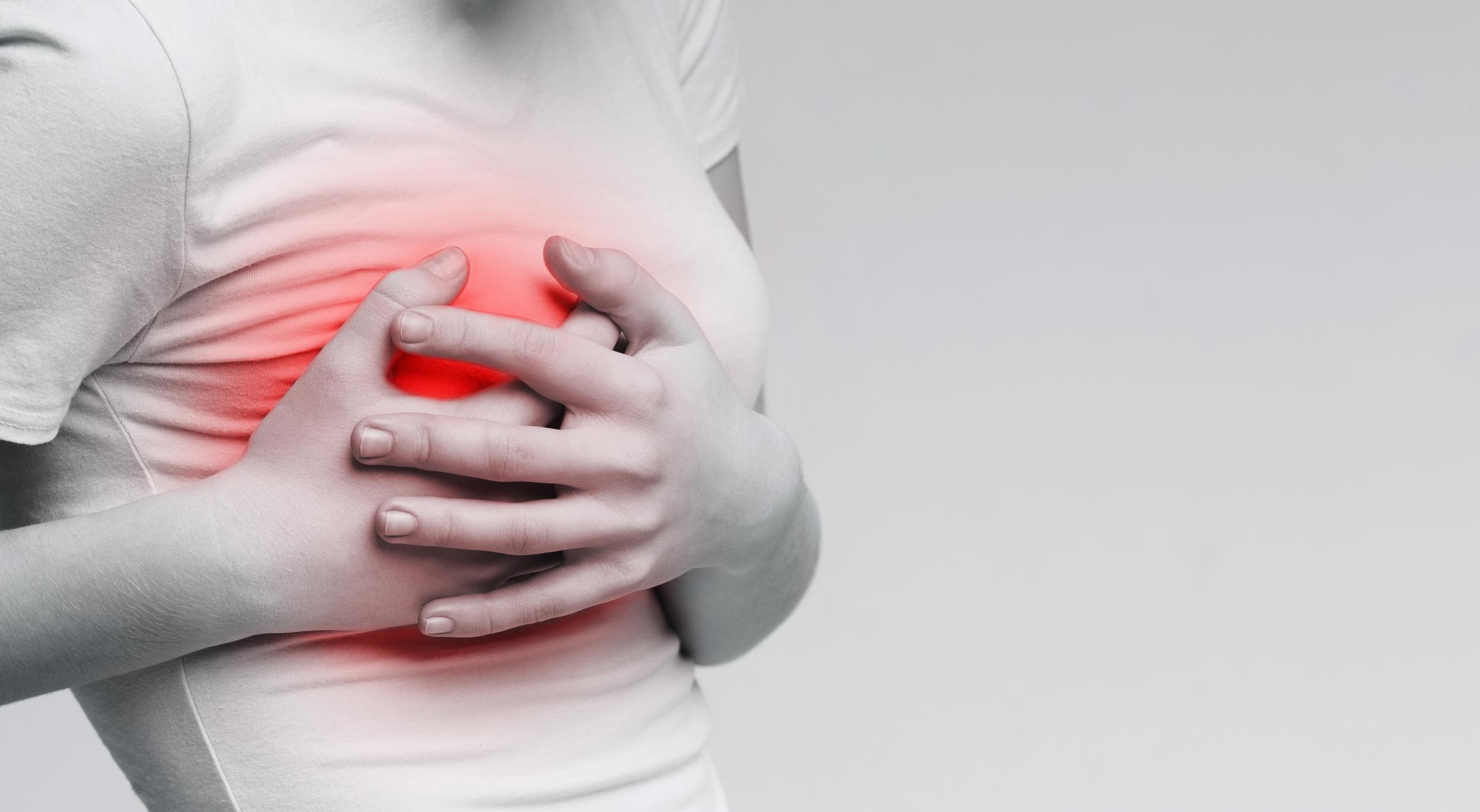 A woman clutching her chest, indicating sudden chest pain—a potential symptom requiring medical evaluation | Source: Getty Images