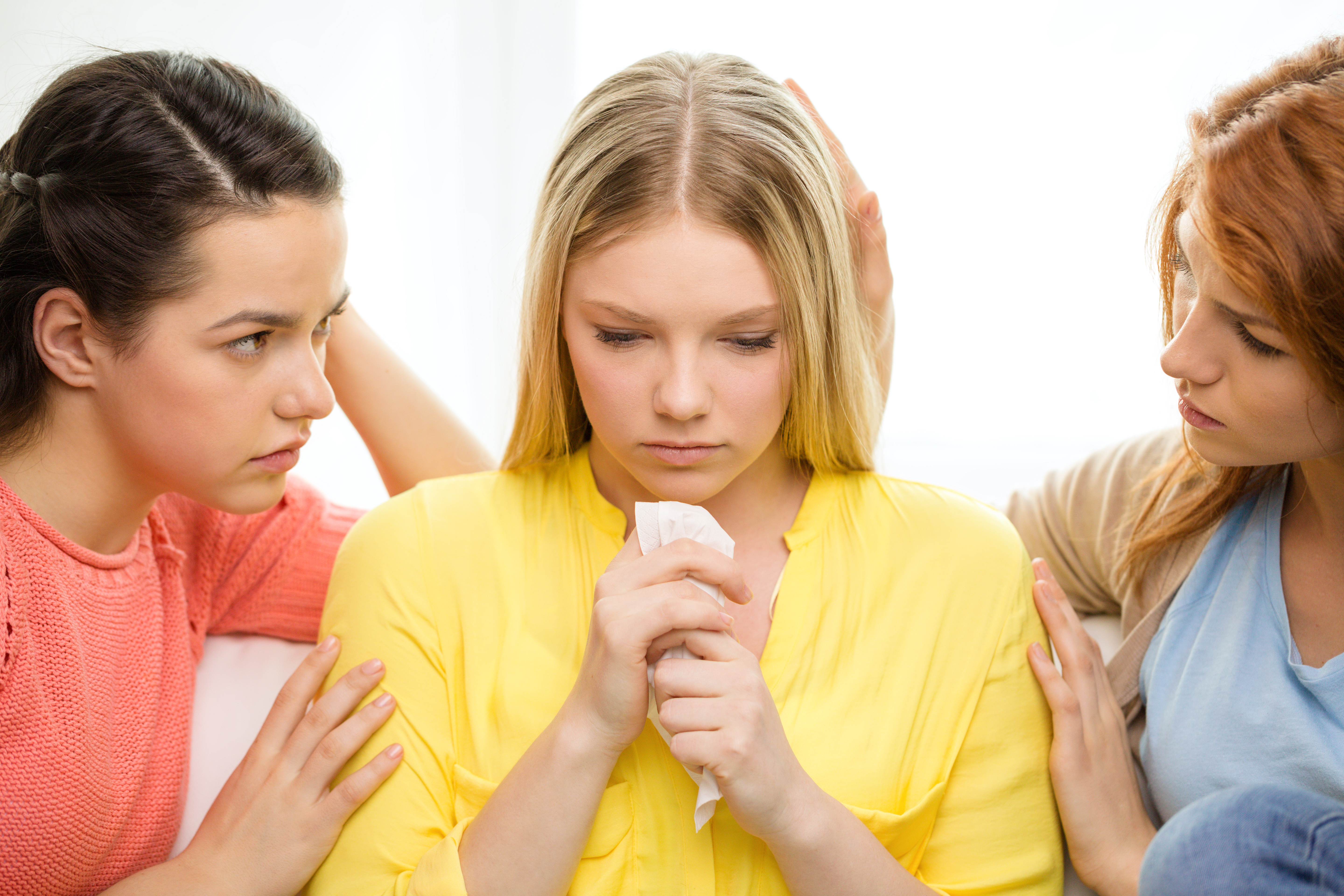 Two girls comforting a girl sitting between them | Source: Shutterstock