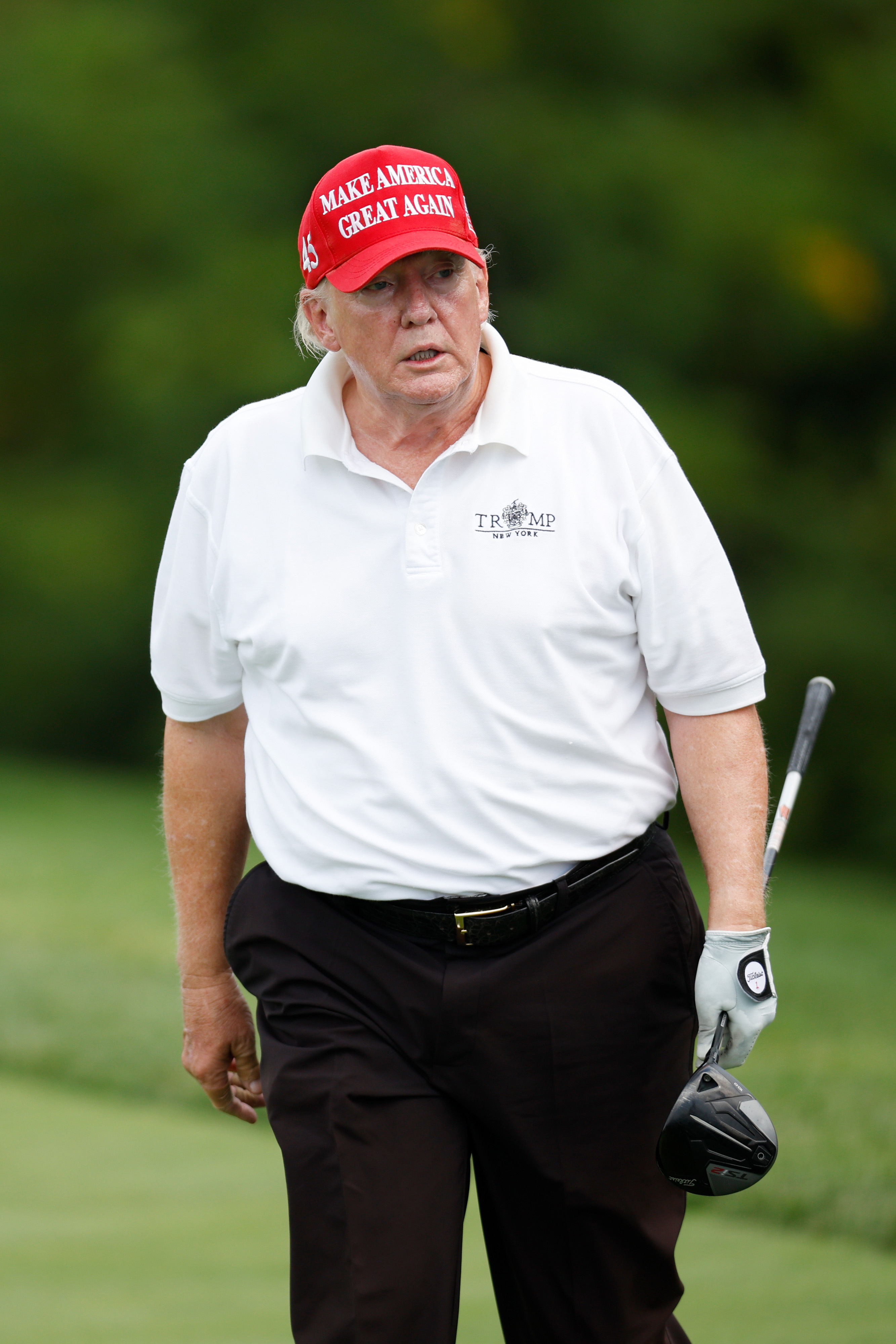 In July 2022, Donald Trump was photographed at the LIV Golf Invitational in Bedminster wearing a white polo and red cap. His face showed uneven skin tones, with no clear signs of makeup.