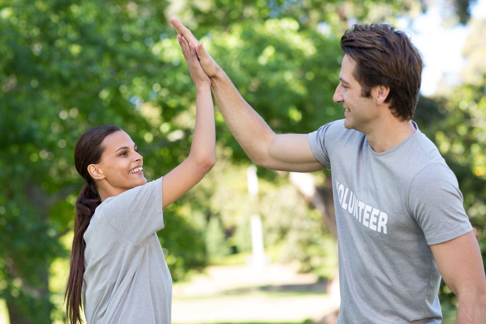 Feliz pareja de voluntarios chocando las manos en un día soleado. | Fuente: Shutterstock