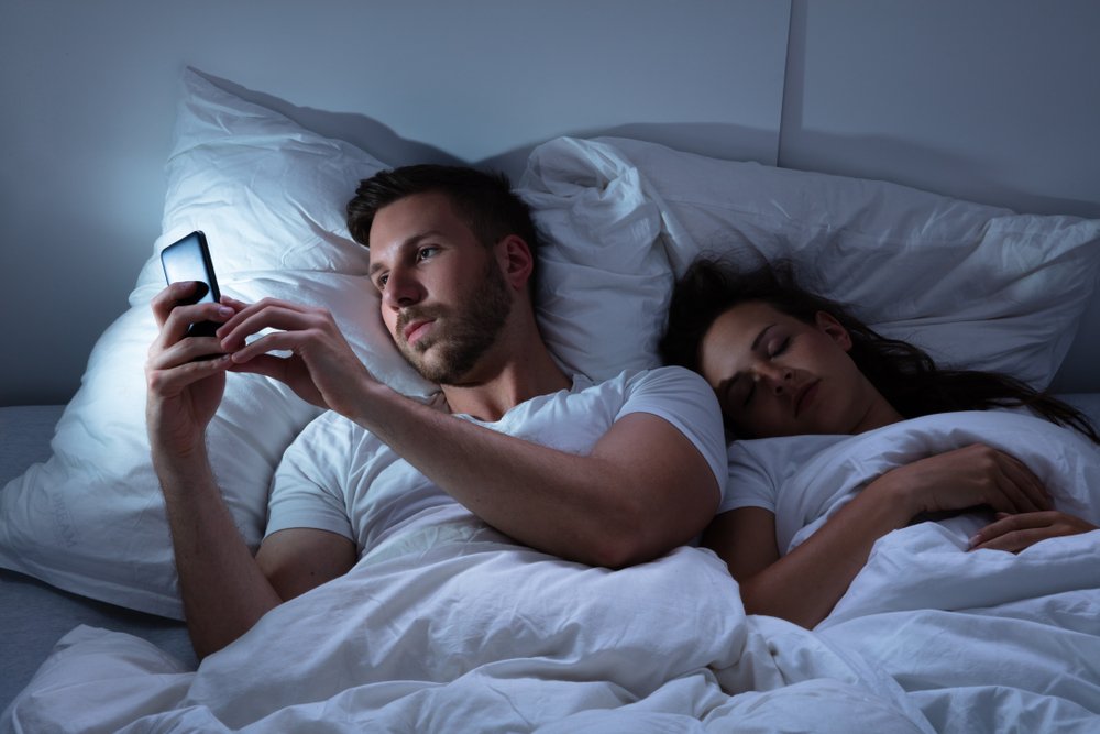 Hombre hablando con su amante mientras su esposa duerme. | Foto: Shutterstock