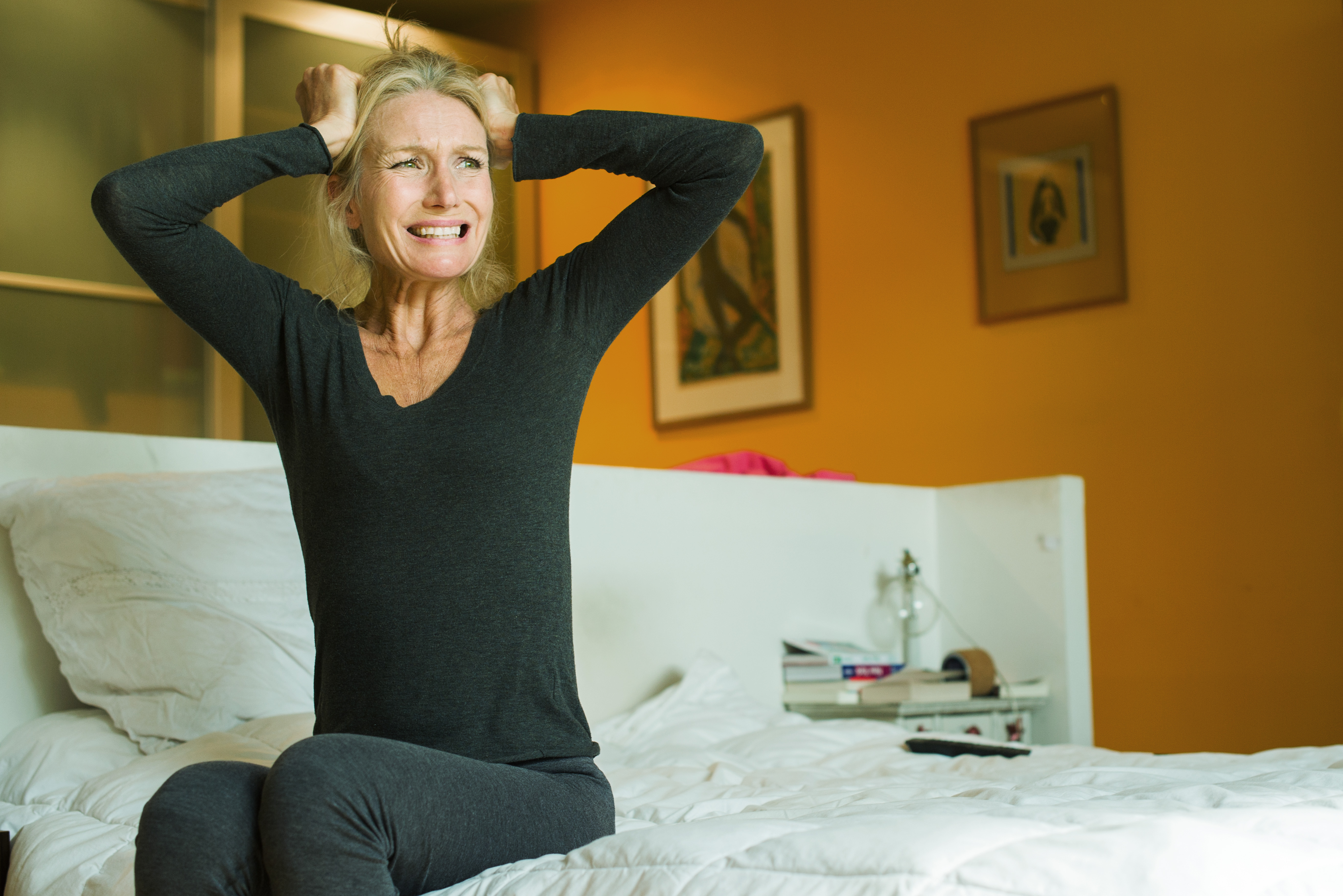 Mature woman sitting on bed with hands on head in exasperation | Source: Getty Images