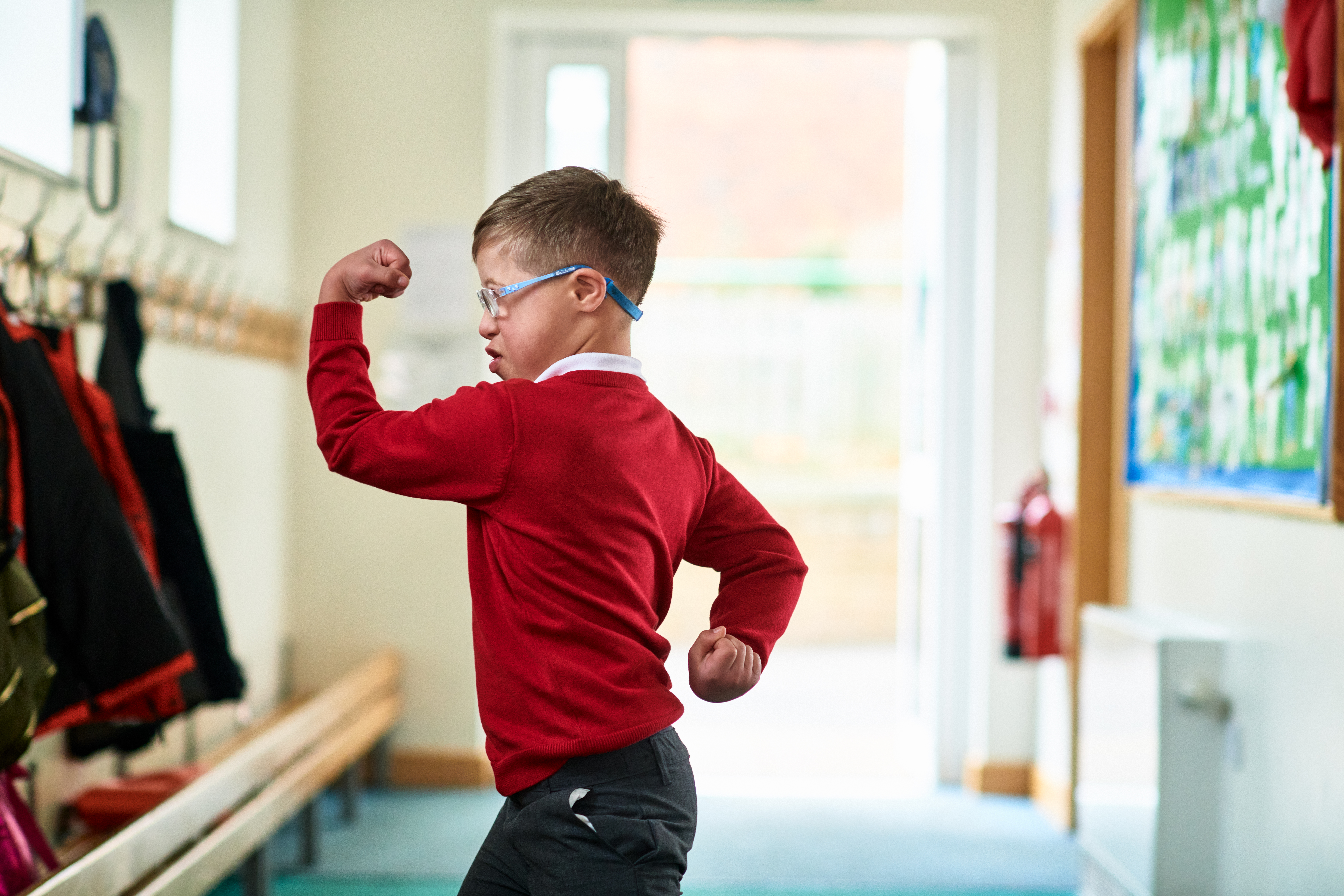 Boy with Down syndrome flexing muscles in school corridor | Source: Getty Images