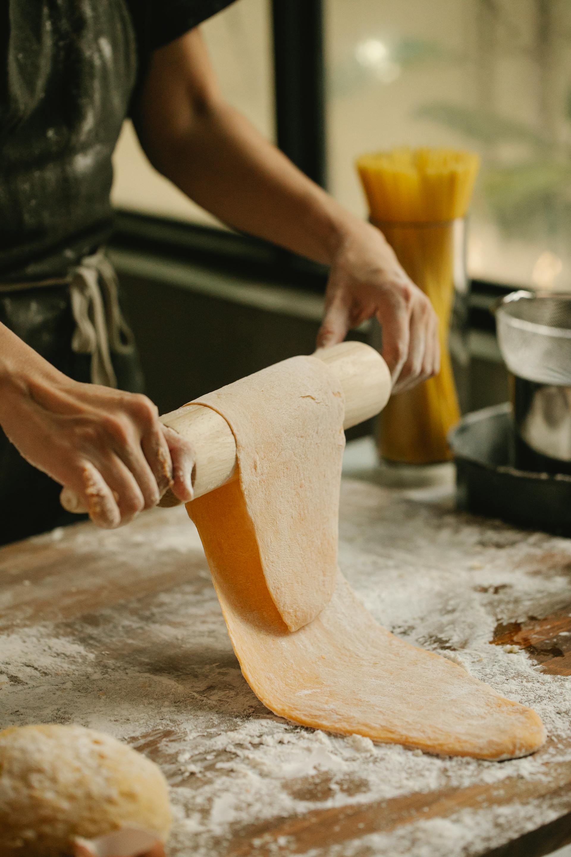 A close-up shot of a young woman rolling pasta dough on floury table at home | Source: Pexels