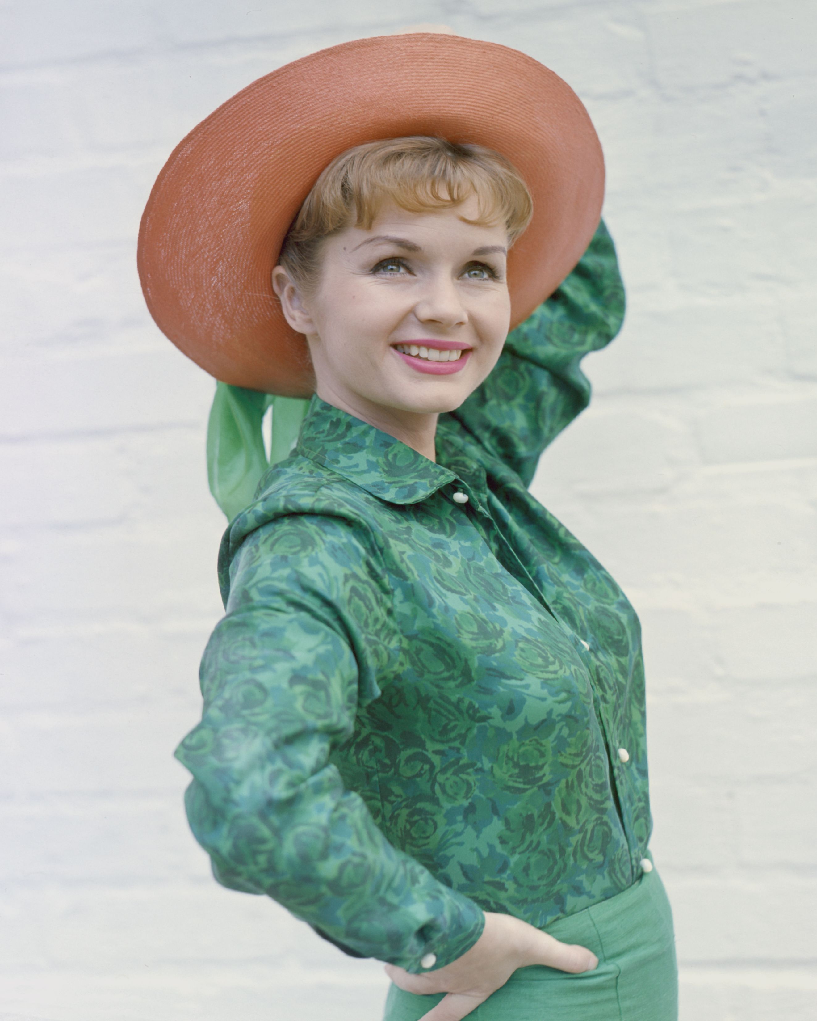 Actress Debbie Reynolds pictured smiling while posing in a green shirt and wide-brimmed salmon pink hat on January 01, 1960 | Photo: Getty Images
