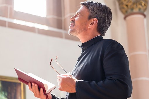 Photo of a priest looking away while holding a bible | Photo: Getty Images