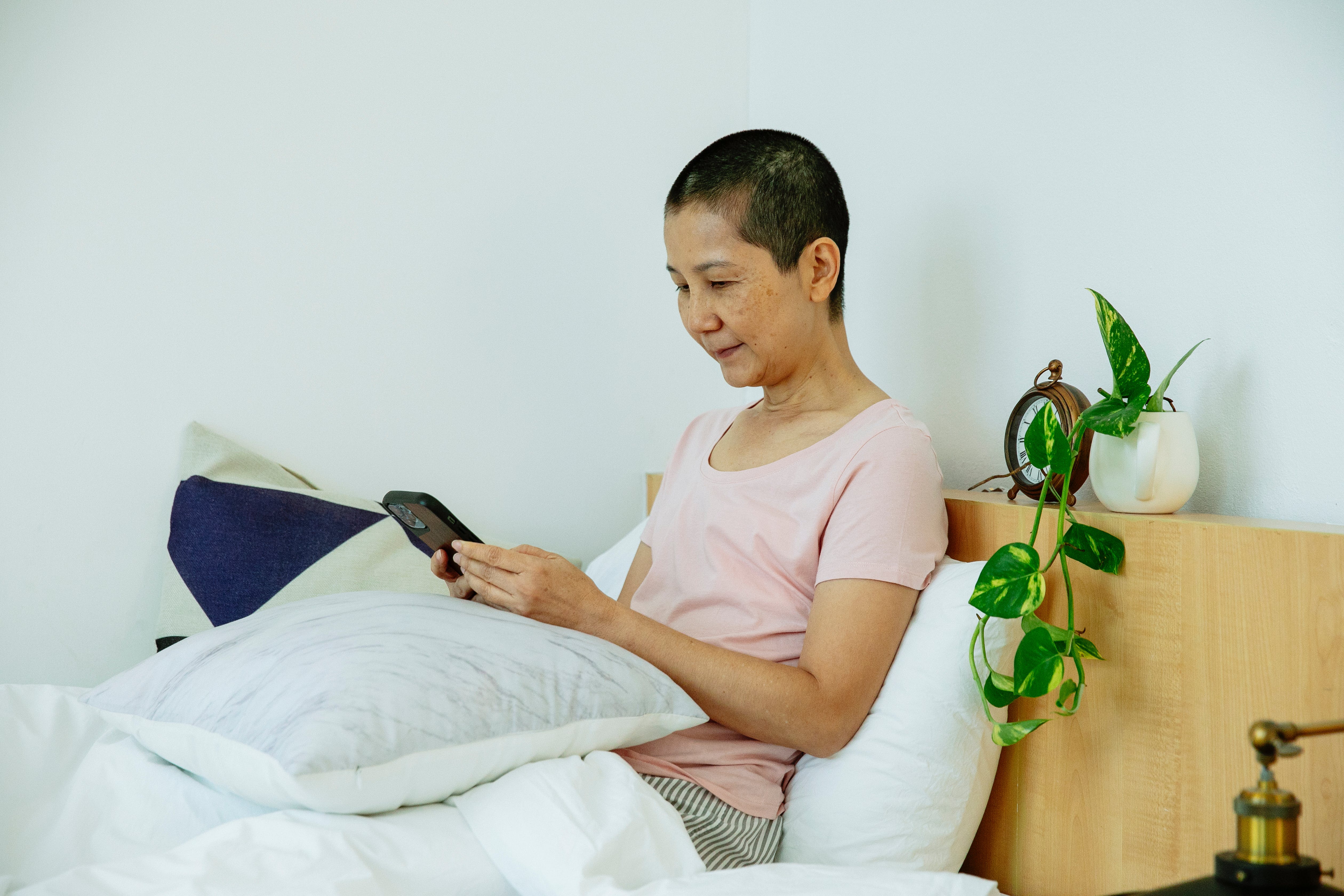 A woman using a smartphone while on the bed┃Source: Pexels