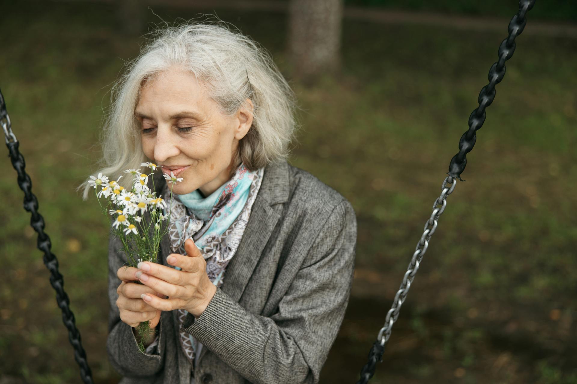 Senior woman sitting on a swing and smelling flowers | Source: Pexels