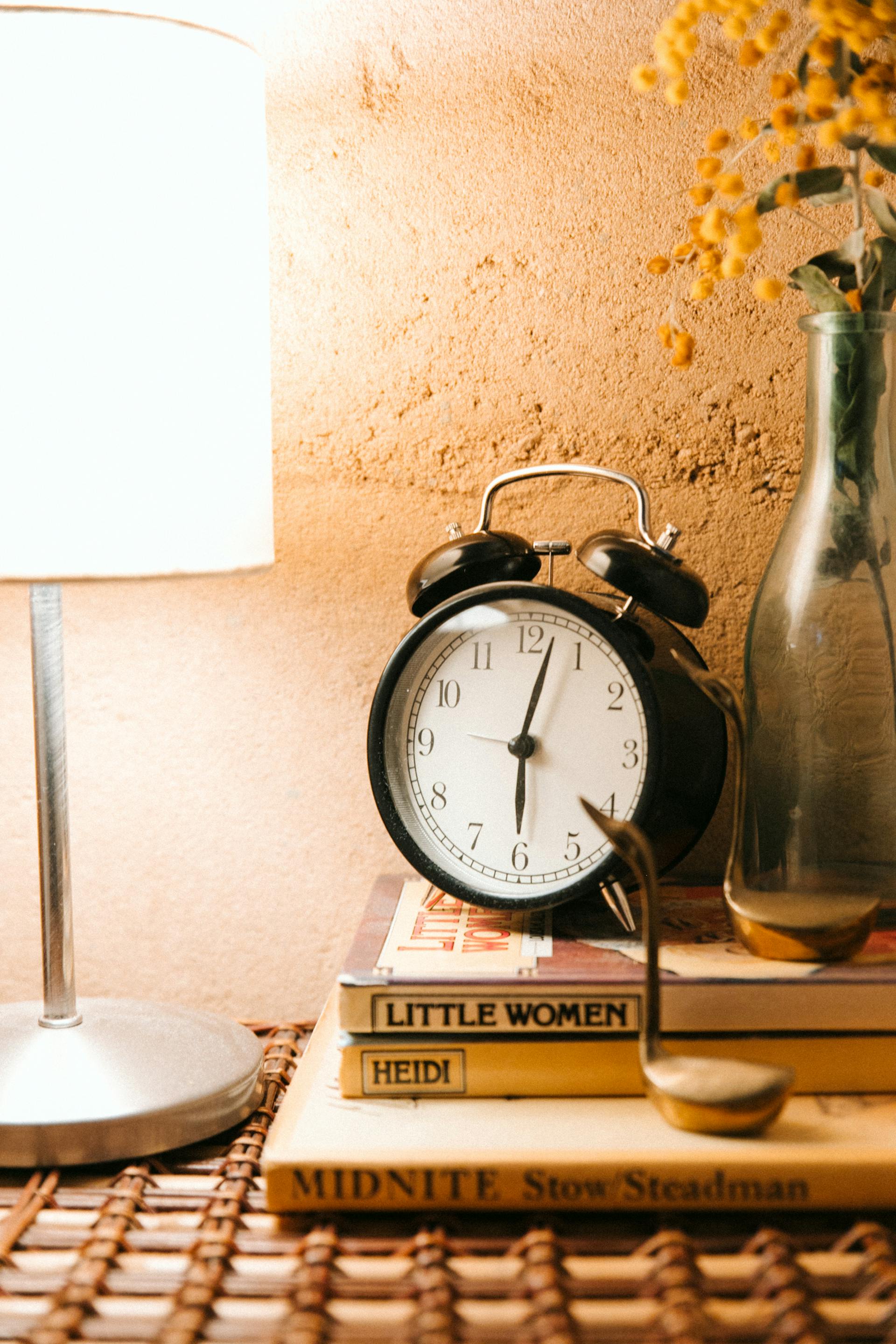 A vintage alarm clock and luminous lamp placed on a bedside table | Source: Pexels