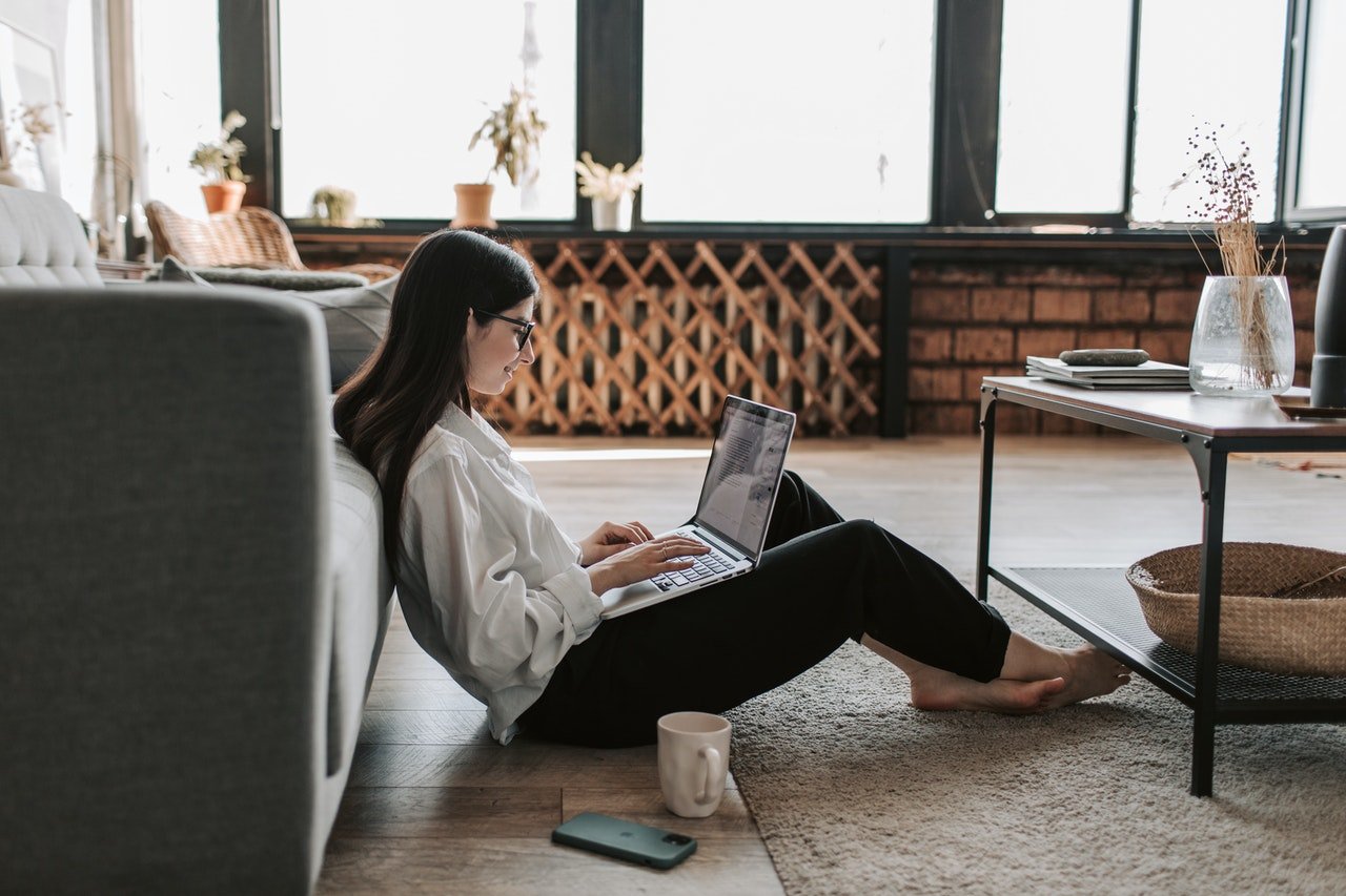 Photo of woman sitting on the floor of her apartment while working on a laptop. | Source: Pexels/Vlada Karpovich