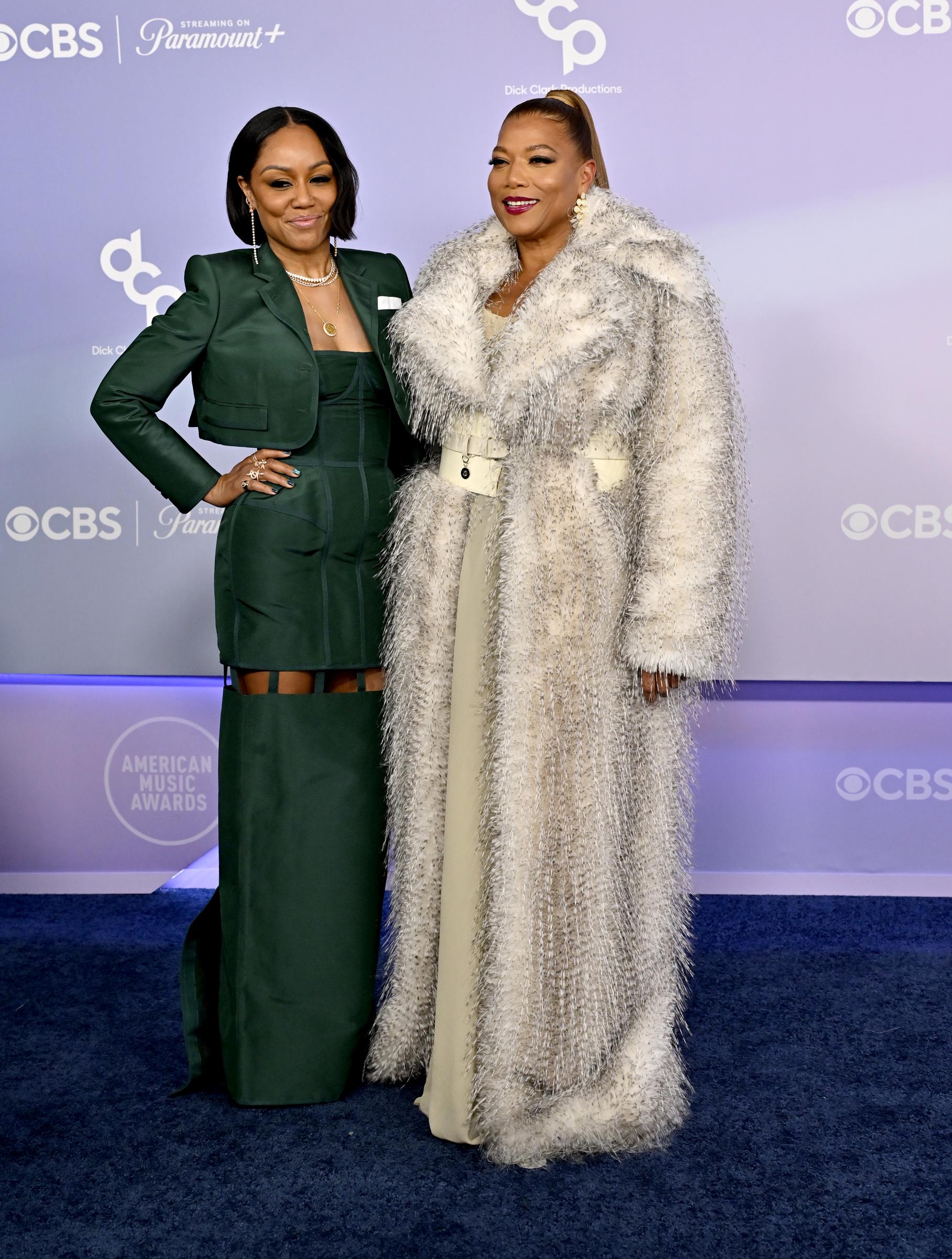 Eboni Nichols and Queen Latifah pause together under bright event lighting while posing in coordinated evening looks at the 2026 American Music Awards in Las Vegas.