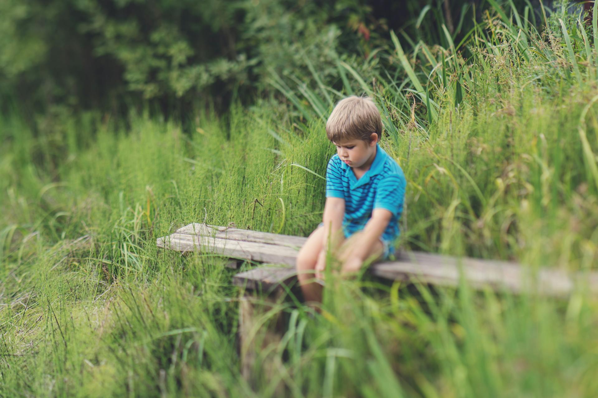 A boy in a blue t-shirt sitting alone on a wooden bench | Source: Pexels