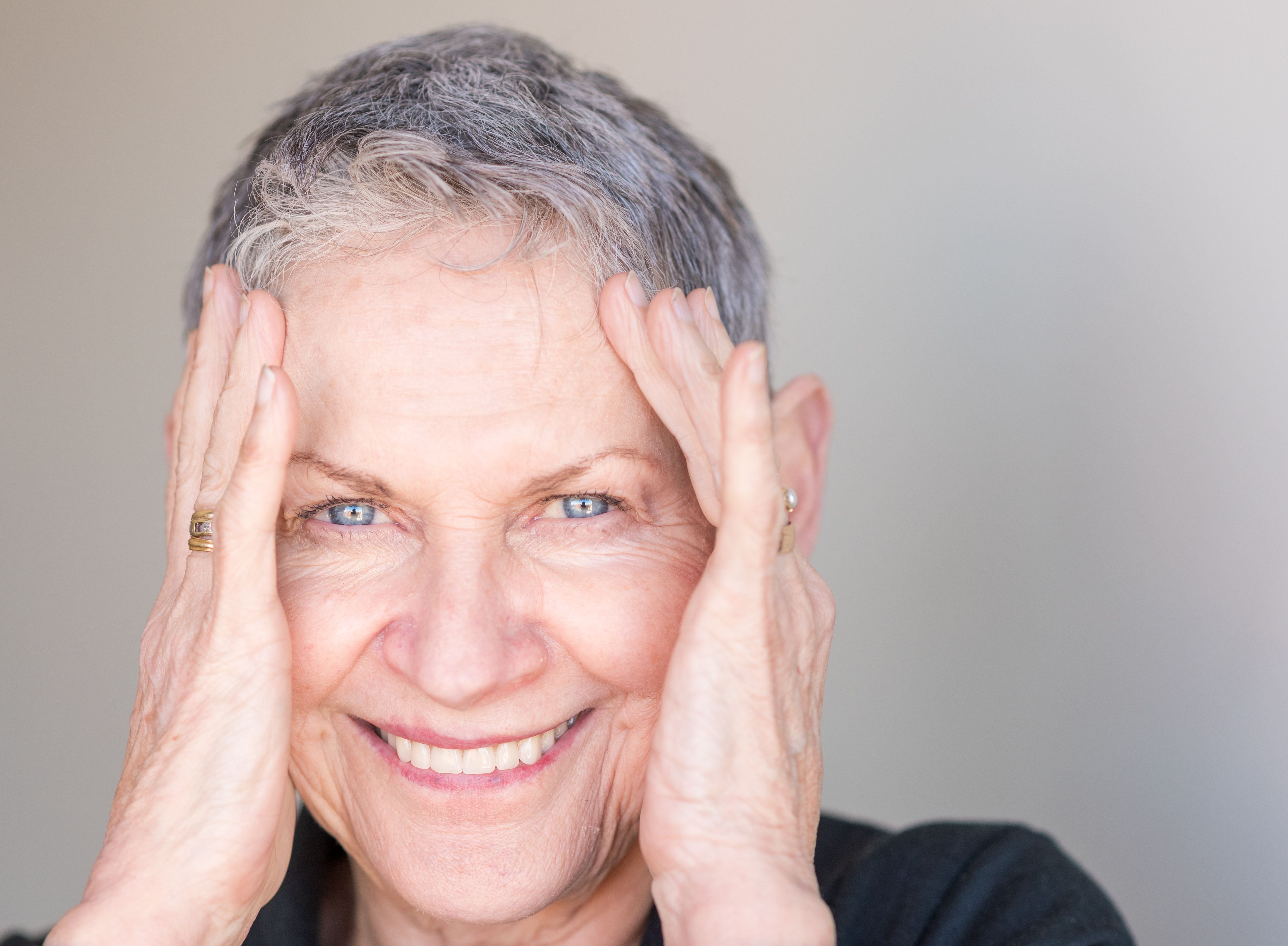 Close up portrait of beautiful older woman with short grey hair smiling with hands around face. | Source: Shutterstock