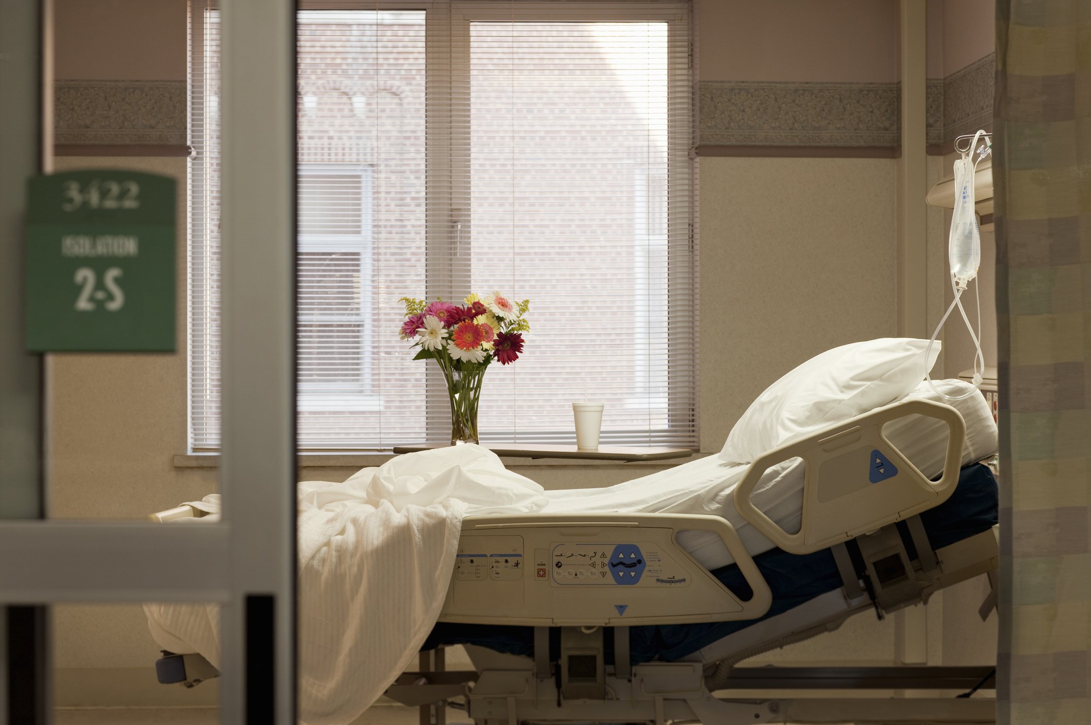 Leeres Krankenhausbett im Zimmer mit Blumen und Infusionsbeutel | Quelle: Getty Images