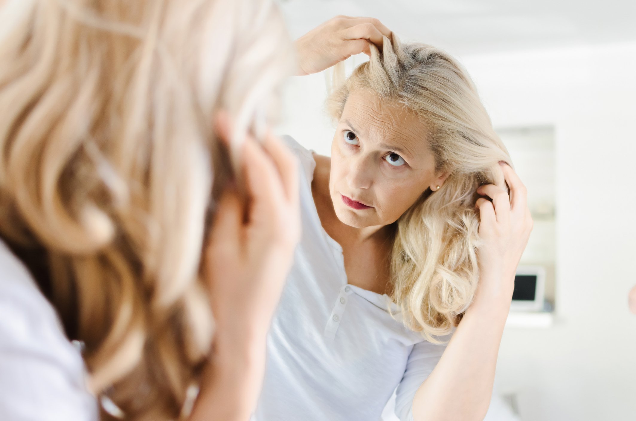 Une femme avec des cheveux blonds regardant dans le miroir. | Photo : Getty Images