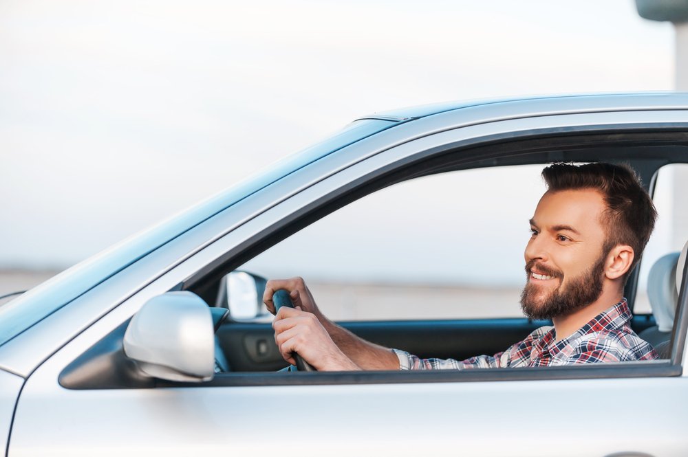 Mann, der lächelnd in einem Auto am Steuer sitzt | Quelle: Shutterstock