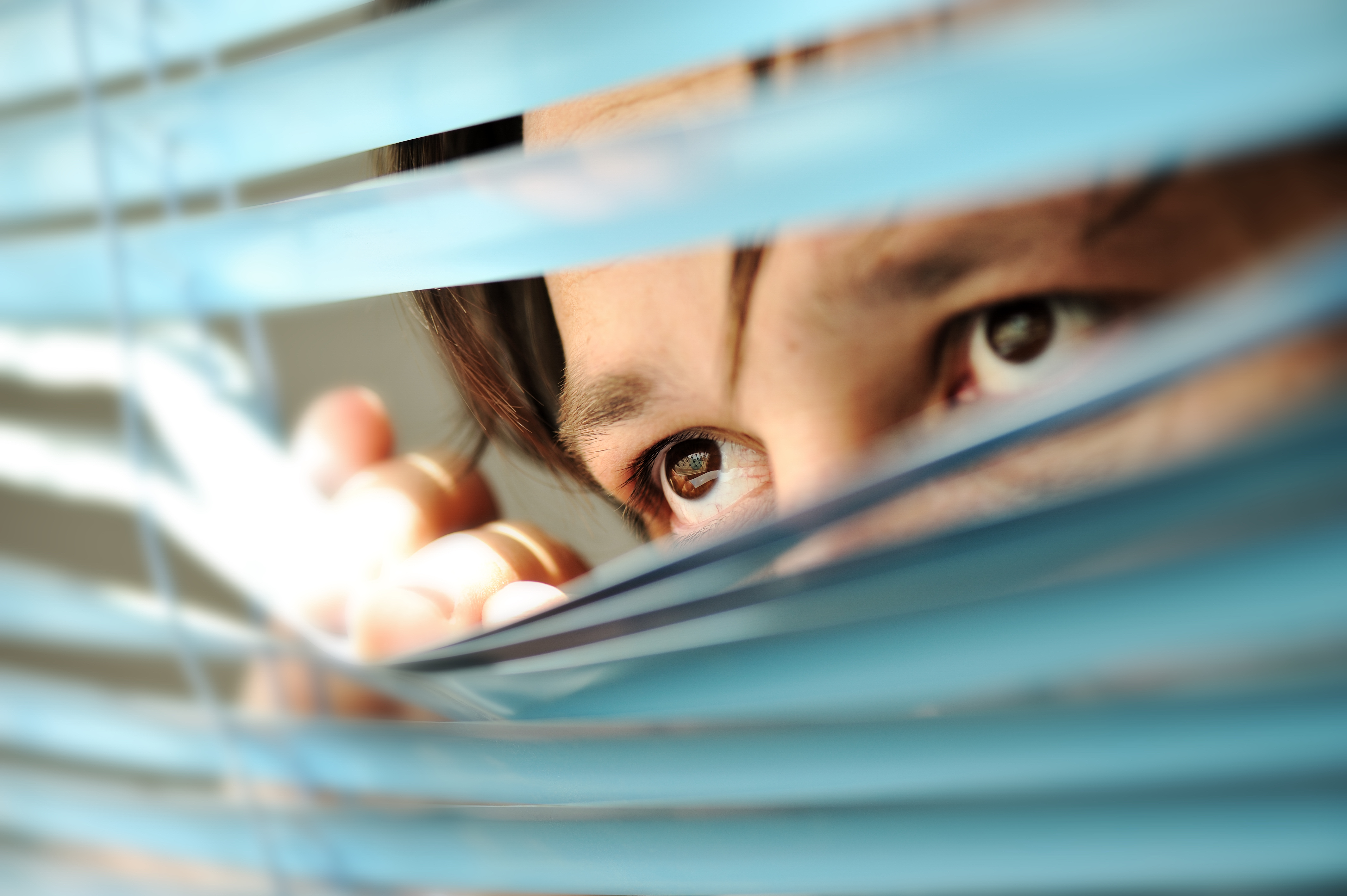 Man looking through window blinds. | Source: Shutterstock