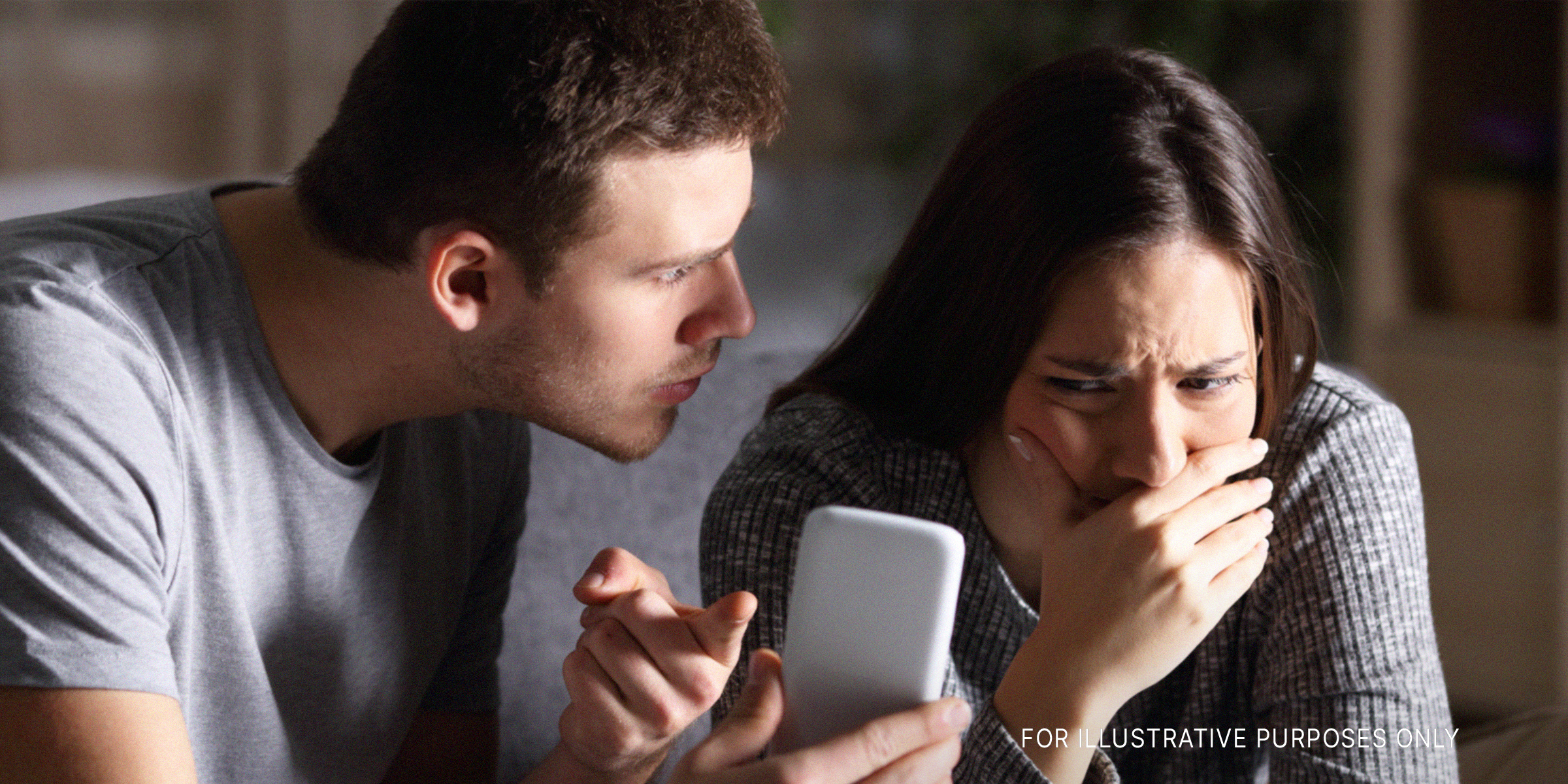 An angry man shows a cell phone to his seemingly embarrassed girlfriend | Source: Shutterstock