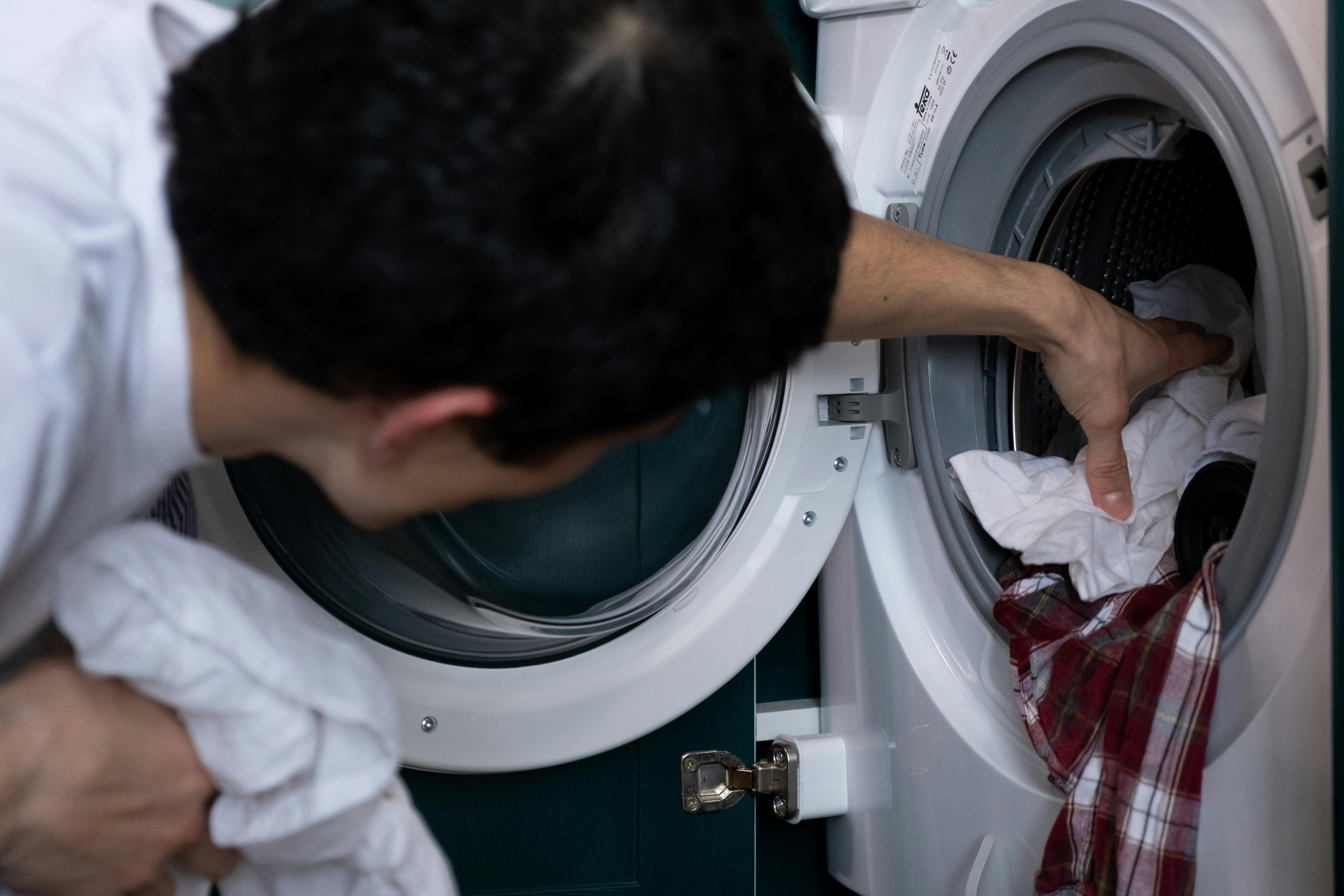 Un hombre poniendo ropa en una lavadora | Fuente: Pexels