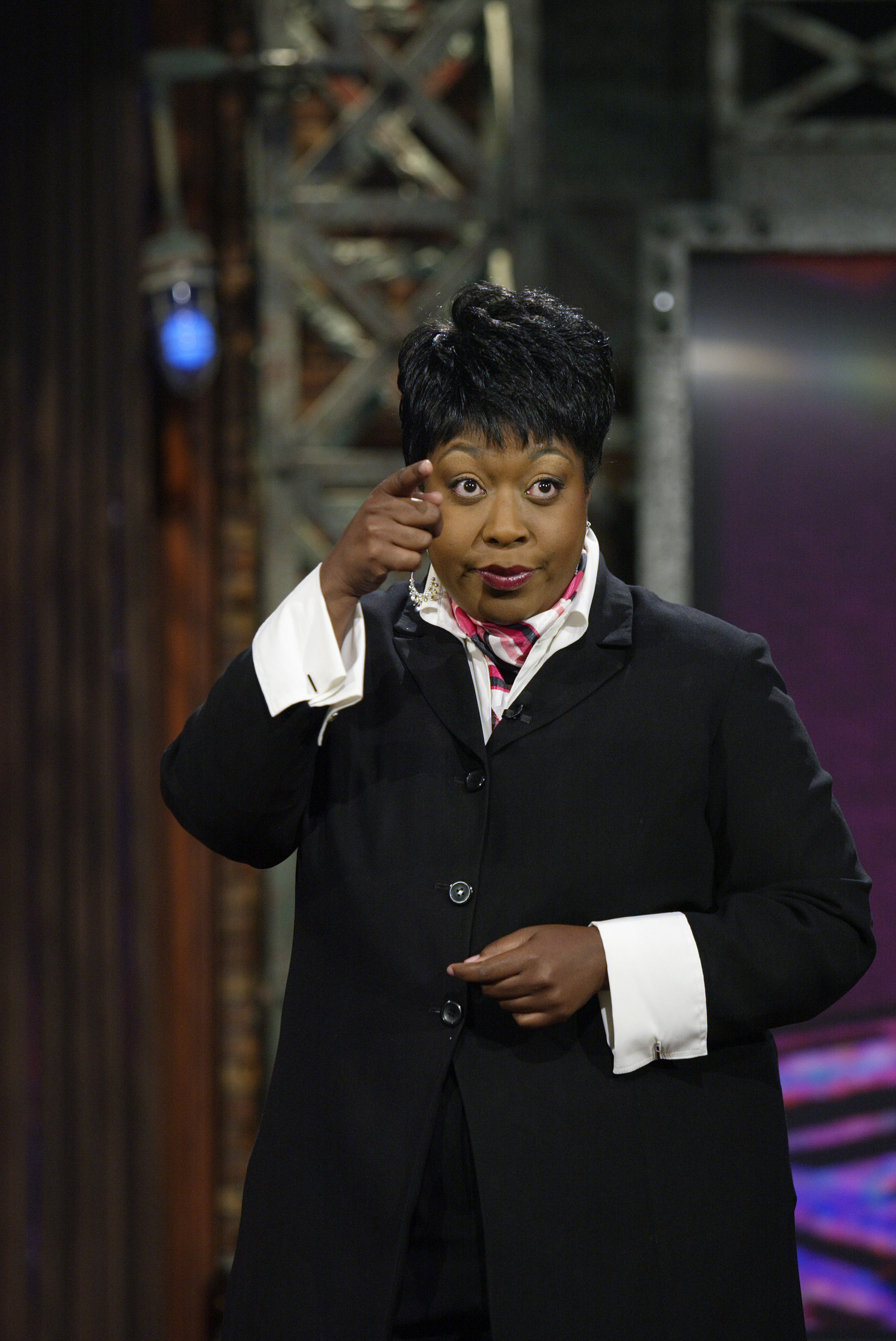 Loni Love performs on "The Tonight Show with Jay Leno" on July 26, wearing a black suit with crisp white cuffs and a patterned scarf as she gestures animatedly during her Season 14 appearance.