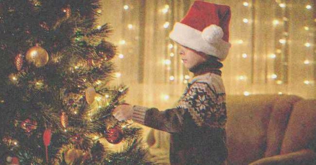 Niño colocando un adorno en un árbol de Navidad | Shutterstock