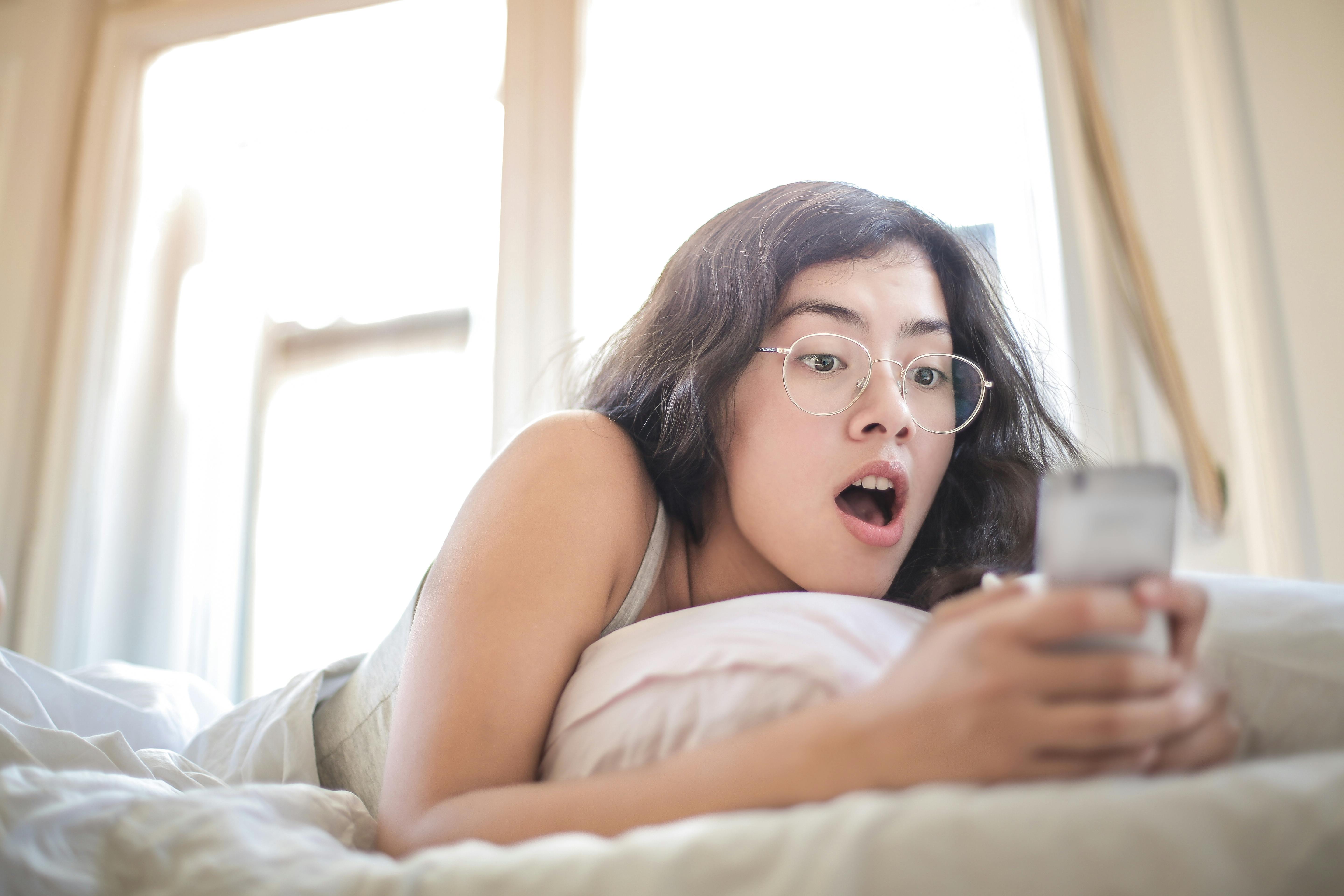 A woman lying on the bed while holding a smartphone | Source: Pexels