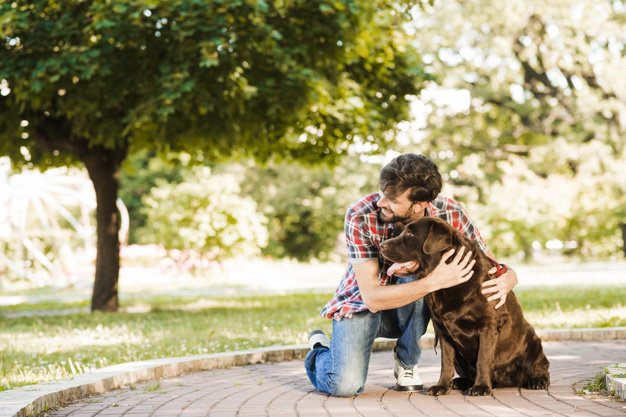 Hombre abrazando a su perro en un jardín. │Foto: Freepik