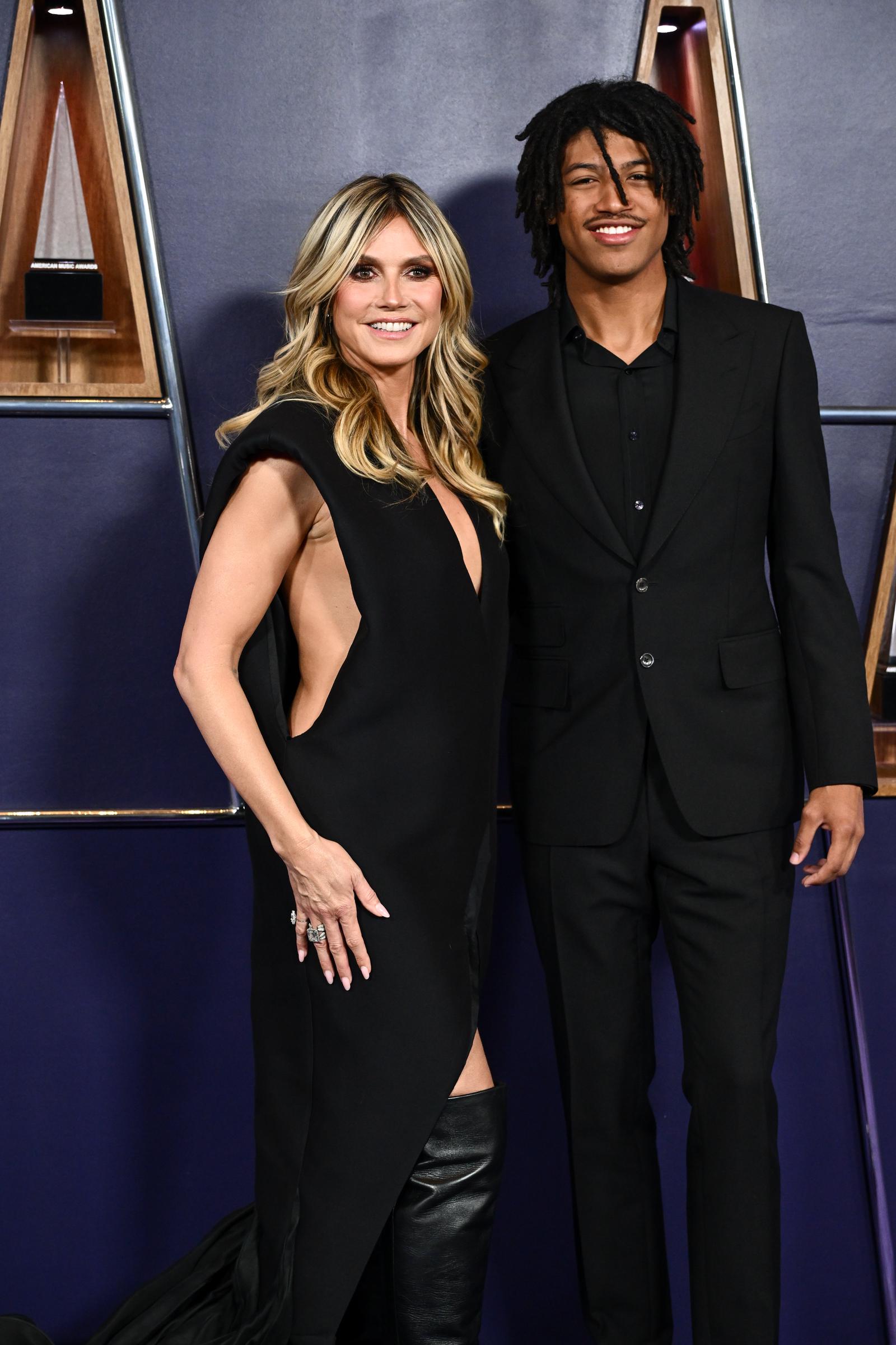 Heidi Klum and her son, Henry Samuel, stand arm-in-arm on the AMAs purple carpet. The sharp lines of her gown and his tailored suit made for a polished family photo under the spotlight.