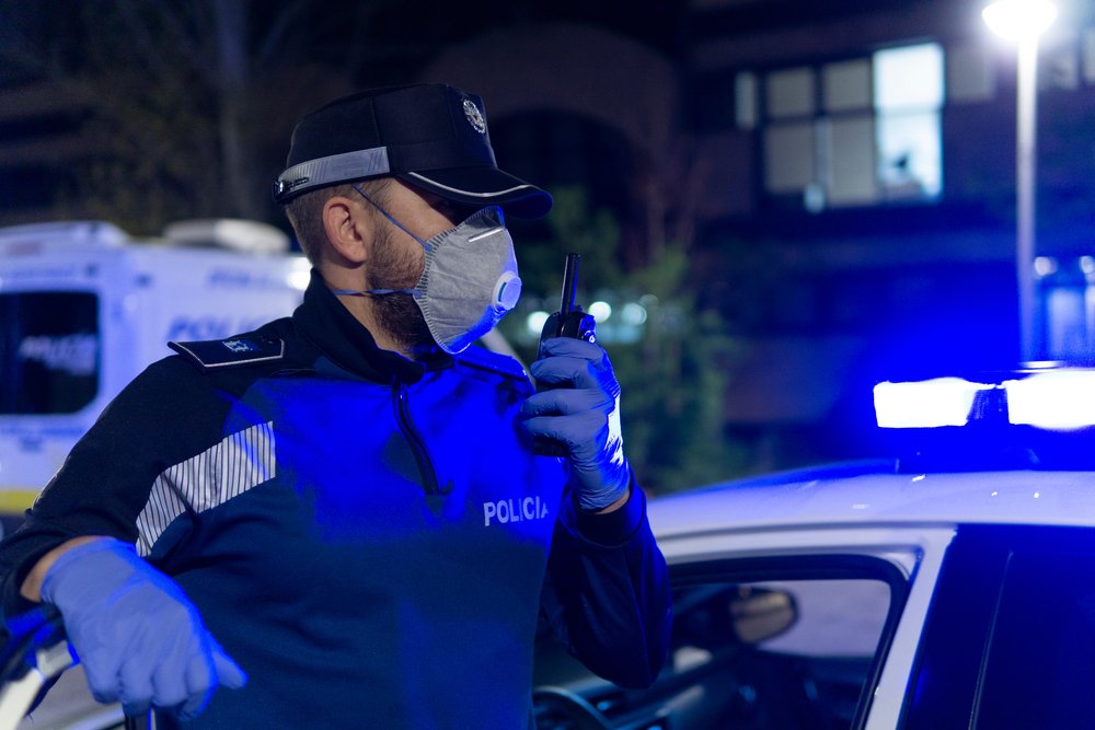A police officer radioing in a call while wearing a face mask and gloves to protect himself from the coronavirus | Photo: Shutterstock/Aitana fotografia