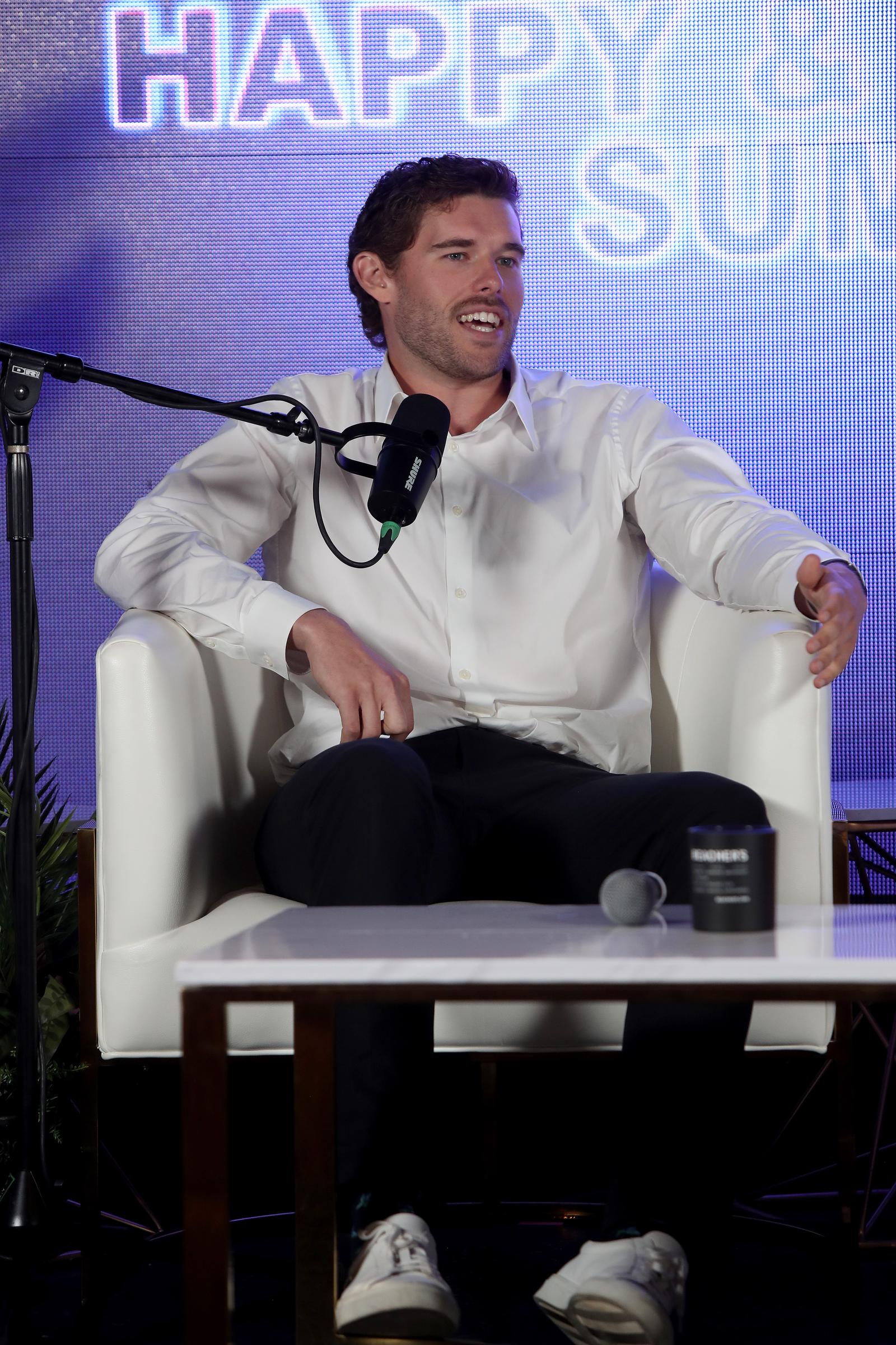 Leaning comfortably into his chair while speaking on stage, Christopher Schwarzenegger shows off his slender silhouette. His trim build and sharp appearance underscore the physical progress he candidly shared with the audience.