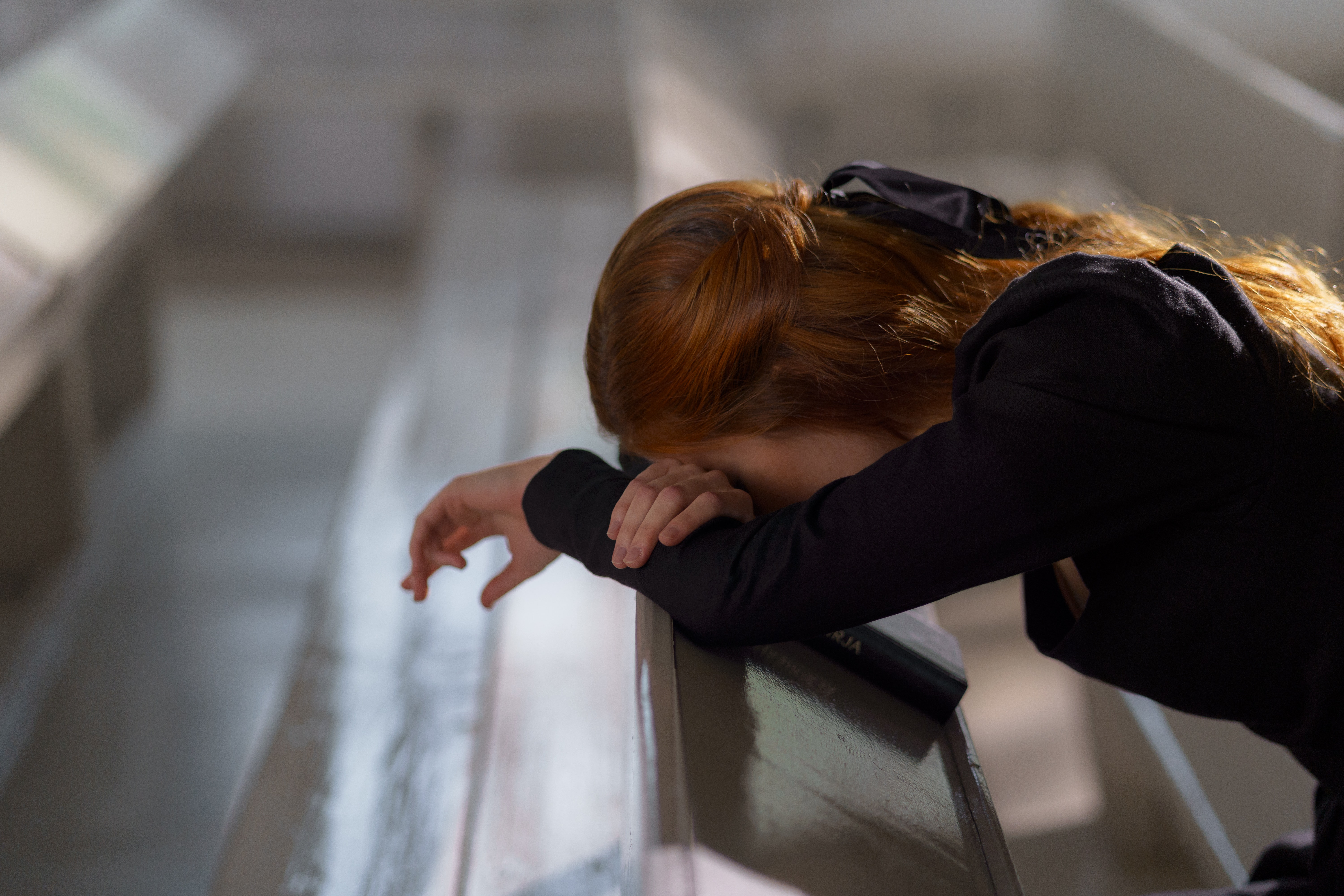 A woman with her head bowed down and leaning on a pew | Source: Pexels