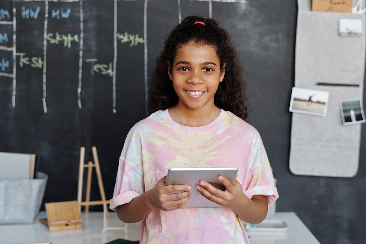 Young school girl smiling while holding a tablet | Photo: Pexels