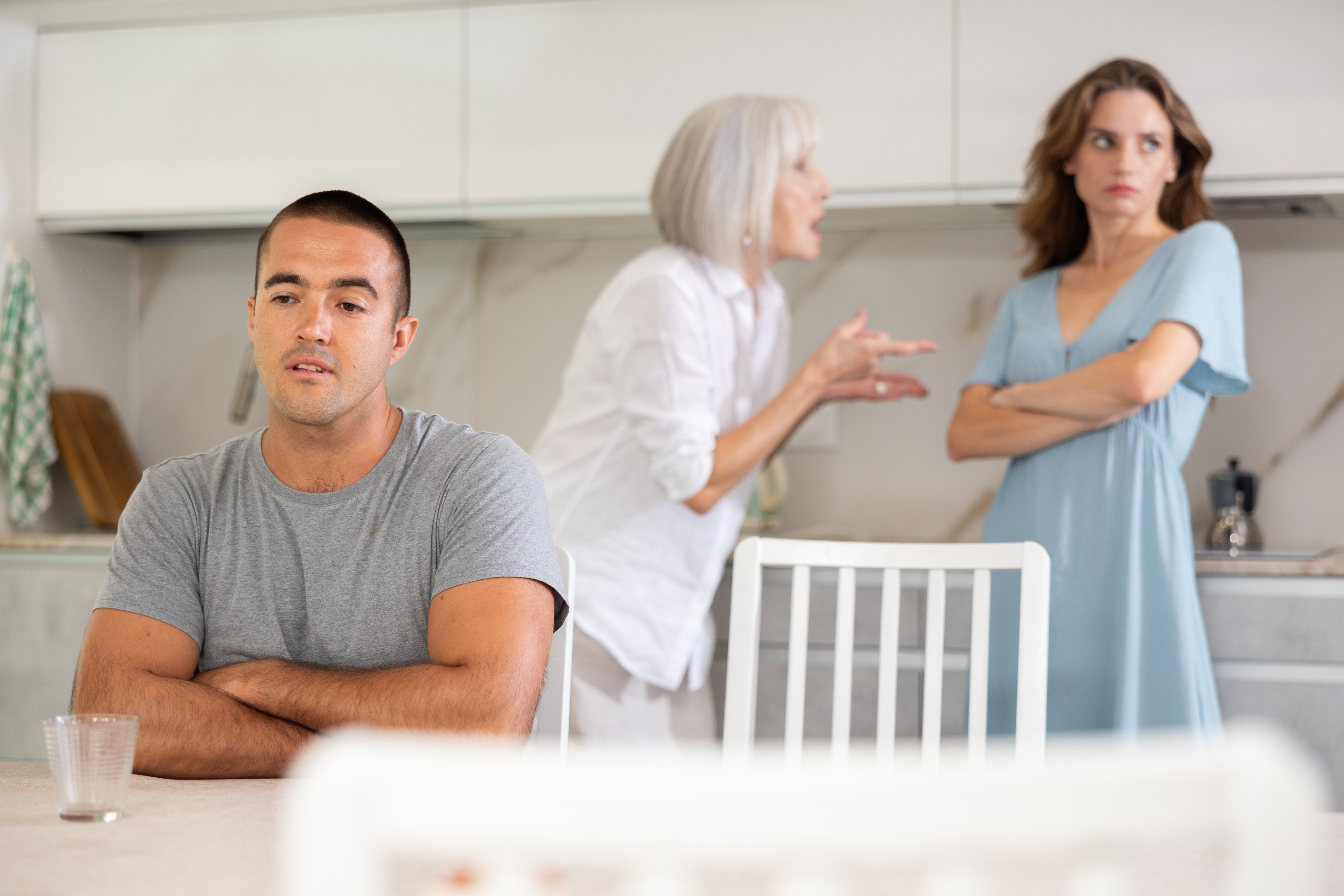 An older woman arguing with a younger woman who looks away as another man sits in front of them | Source: Shutterstock