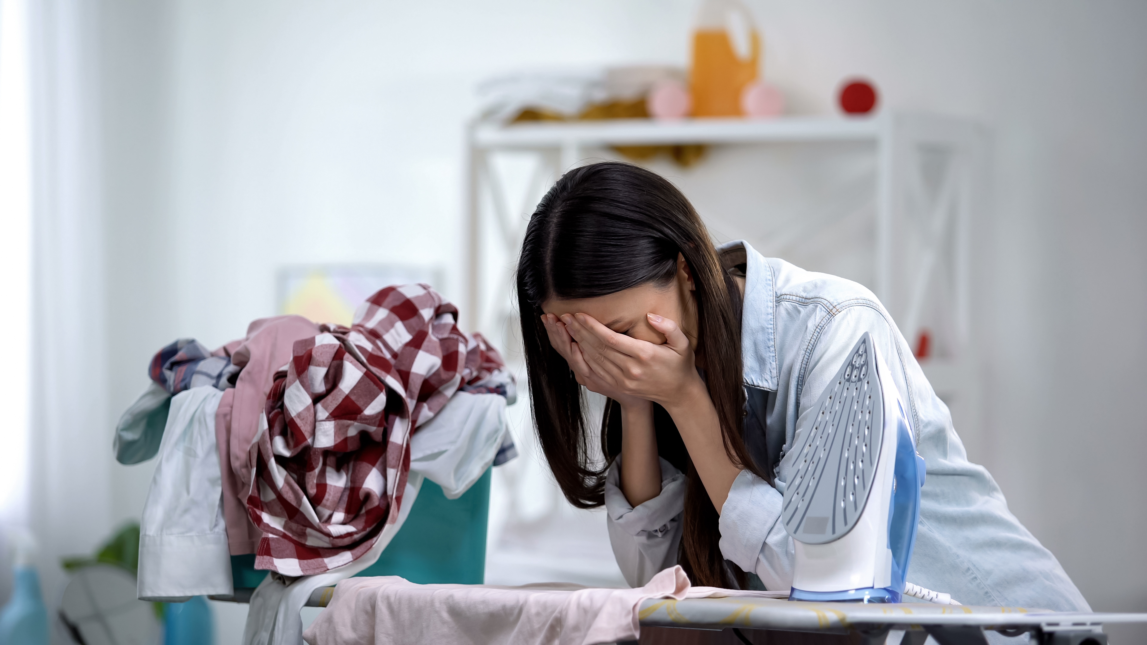 A stressed woman is pictured crying while leaning on the ironing board | Source: Shutterstock